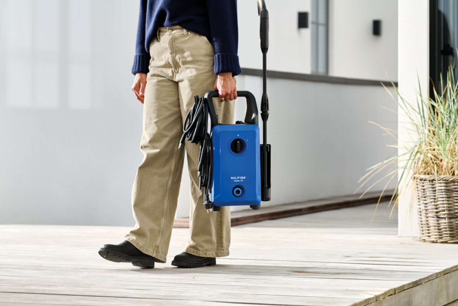 Person in khaki pants holds a blue pressure washer.