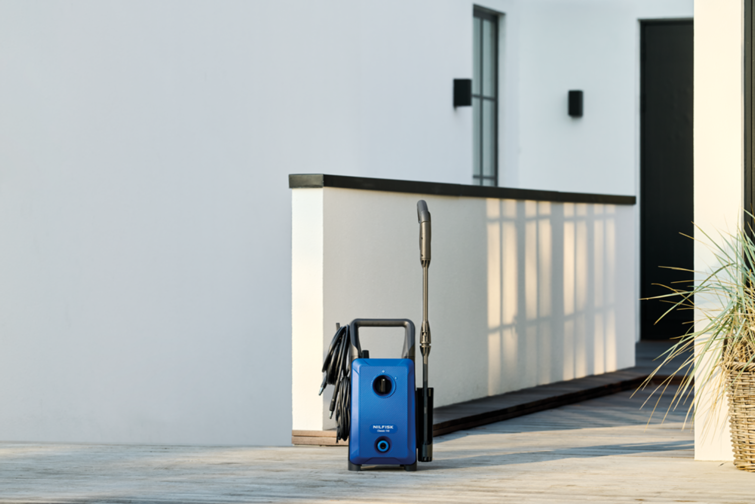 Een blauwe hogedrukreiniger staat op een betonnen vloer naast een wit gebouw.