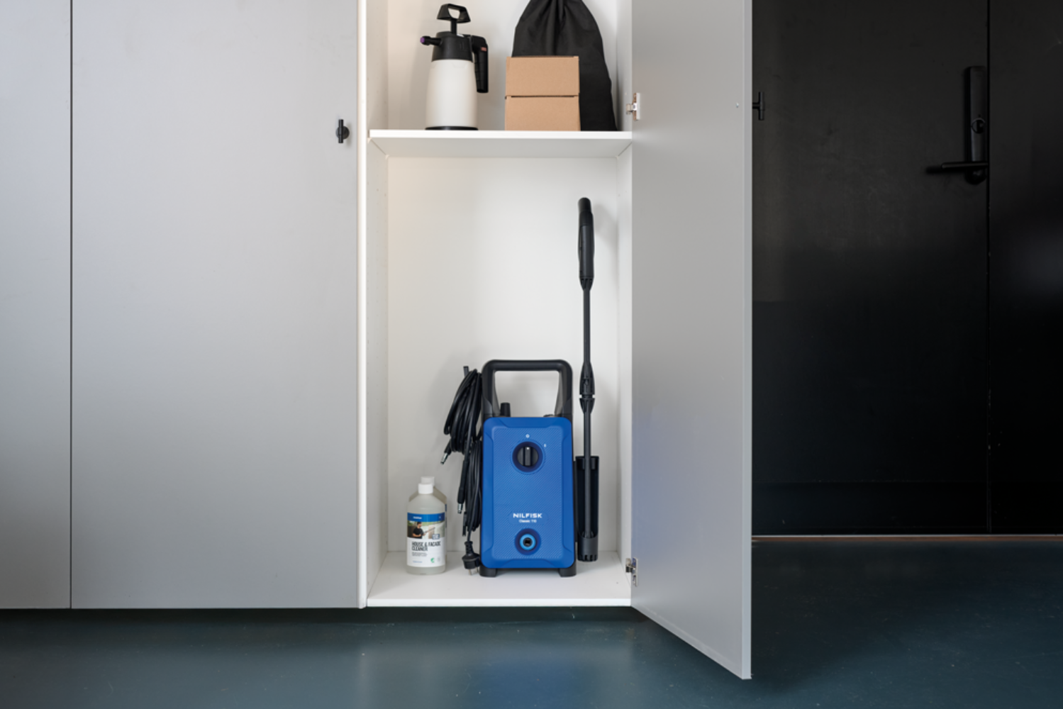 A blue pressure washer stands in an open cabinet next to a bottle of cleaning solution.