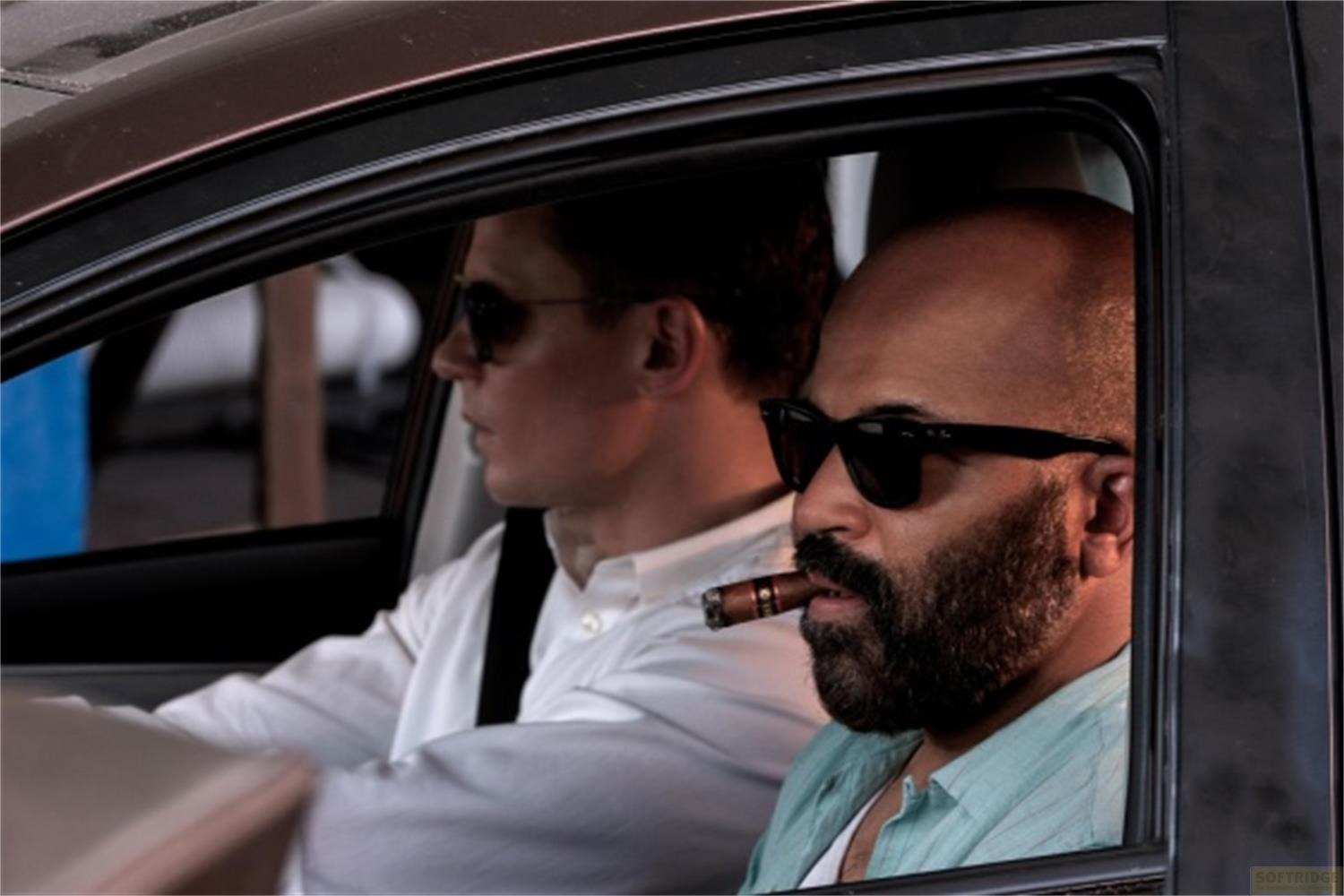 Due uomini con occhiali da sole guidano un'auto, uno fuma un sigaro.