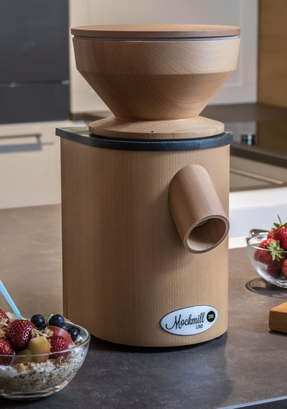 Holzgetreidemühle mit Obstschale und Erdbeeren daneben.