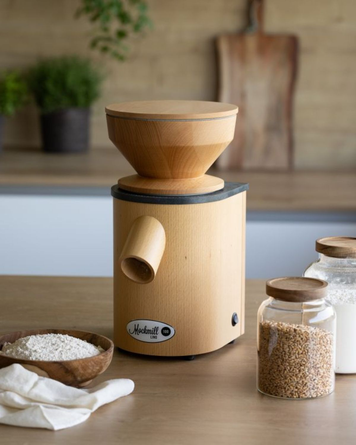 Holzgetreidemühle mit Schüssel Mehl, Weizen und Stoff auf Holztisch.