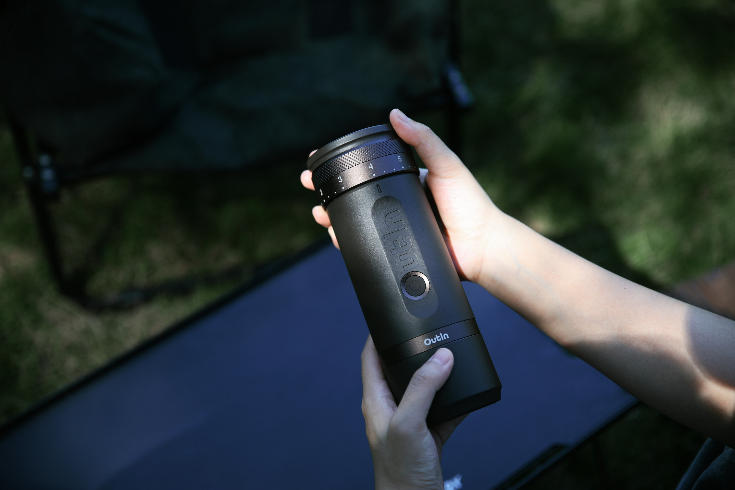 Dłoń trzyma czarny młynek do kawy ze skalą. Na zewnątrz.