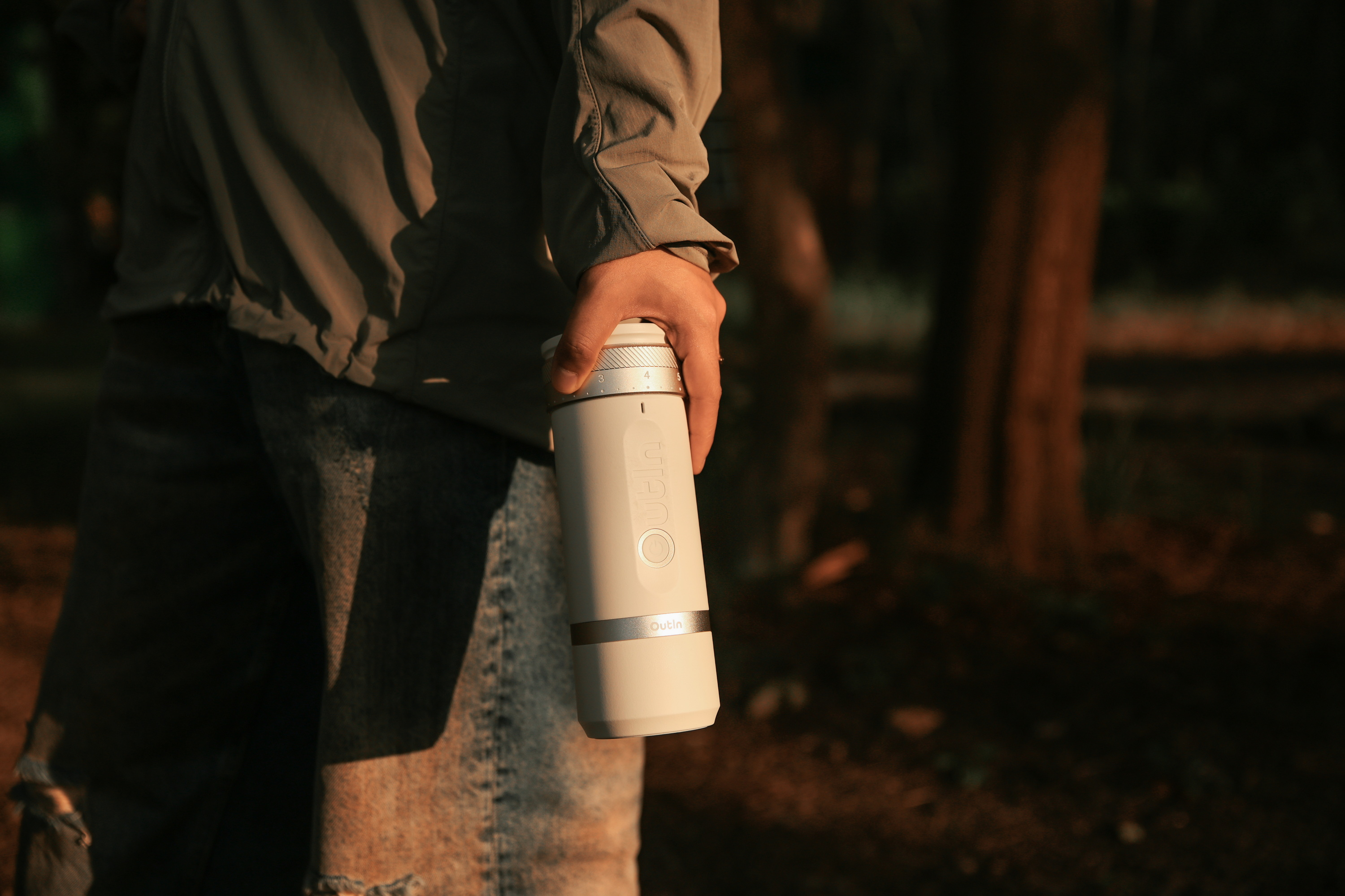 Dłoń trzyma biały kubek do kawy ze srebrnymi pierścieniami i oznaczeniami.