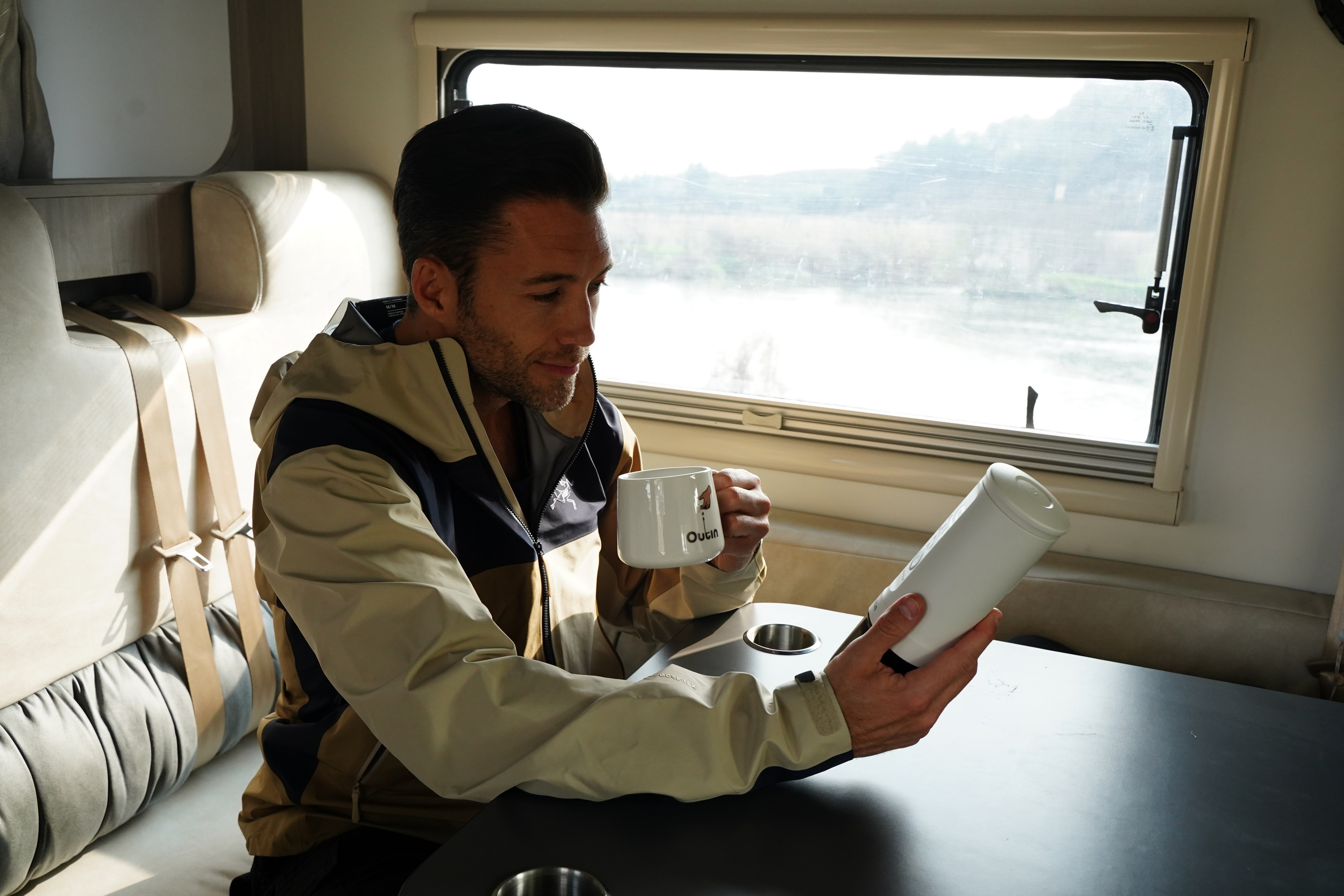 Mann in Wohnmobil hält Tasse und Flasche, schaut aus Fenster auf Landschaft.