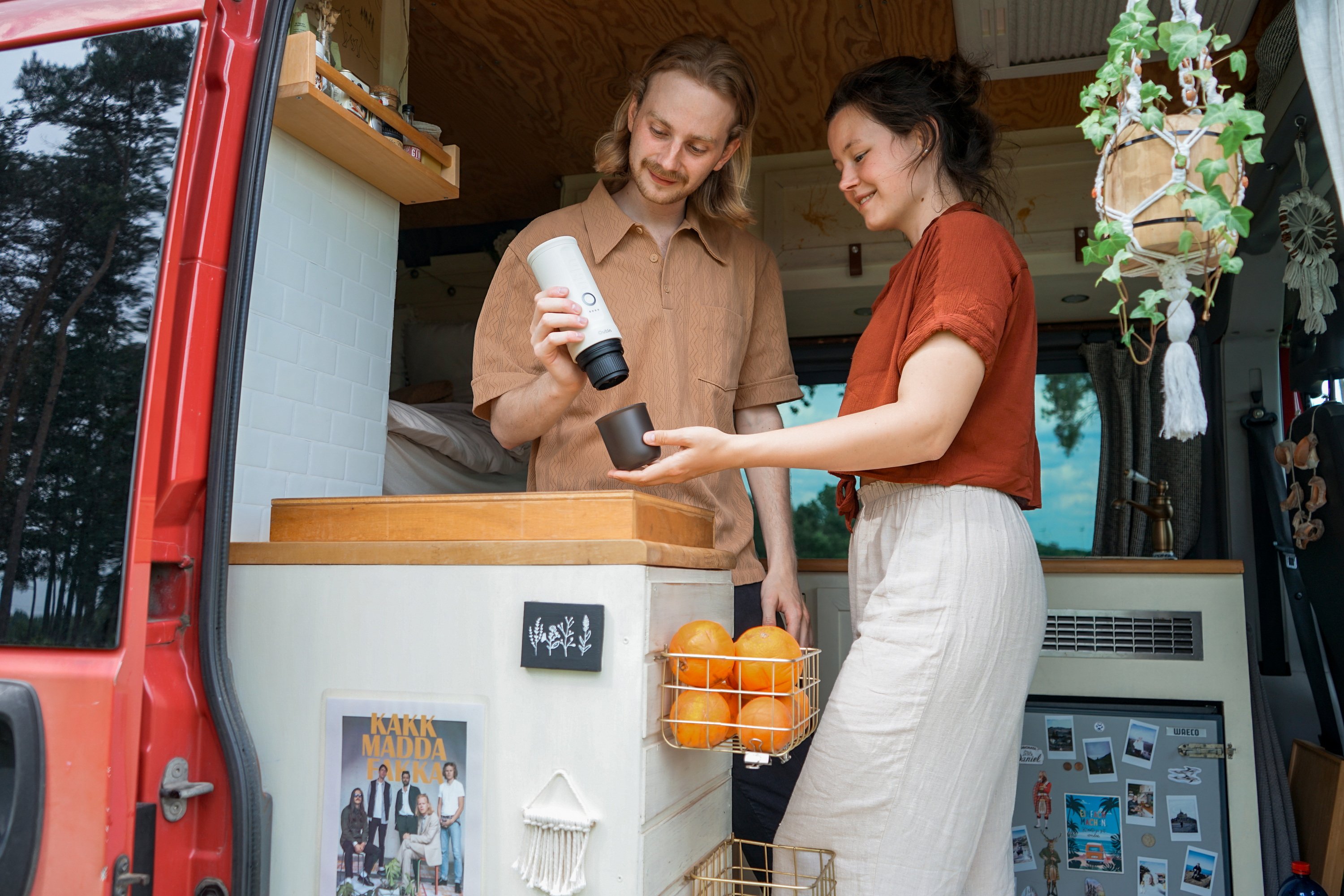Mann und Frau in einem Van, der Mann hält eine Kaffeemaschine, sie eine Tasse.