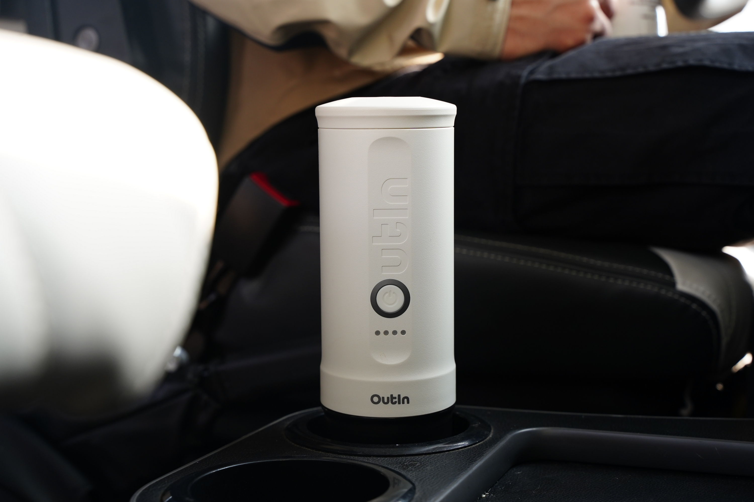 Biały kubek z logo "Outln" w uchwycie na kubek w samochodzie.