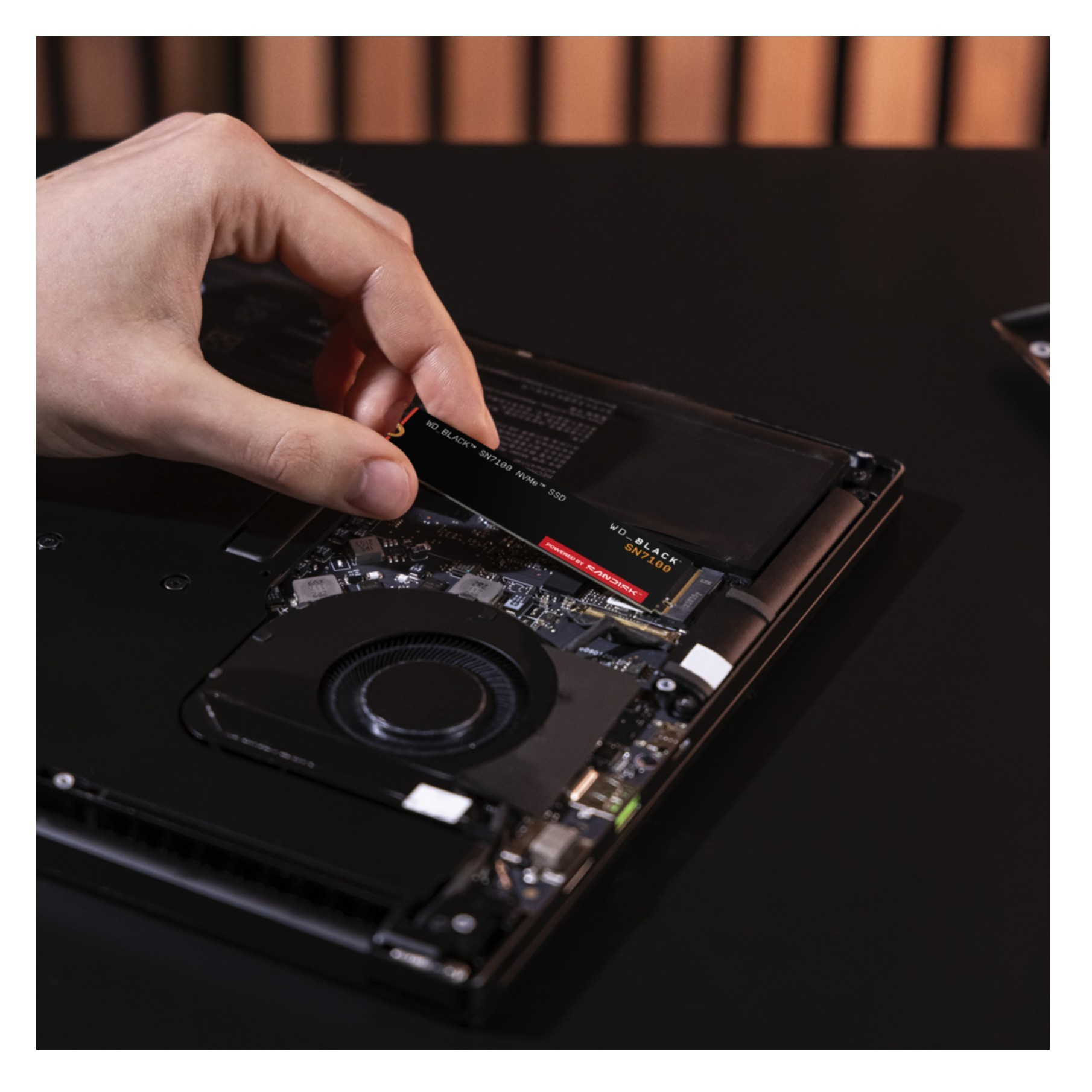 Dłoń instaluje czarny dysk SSD w otwartej obudowie laptopa.