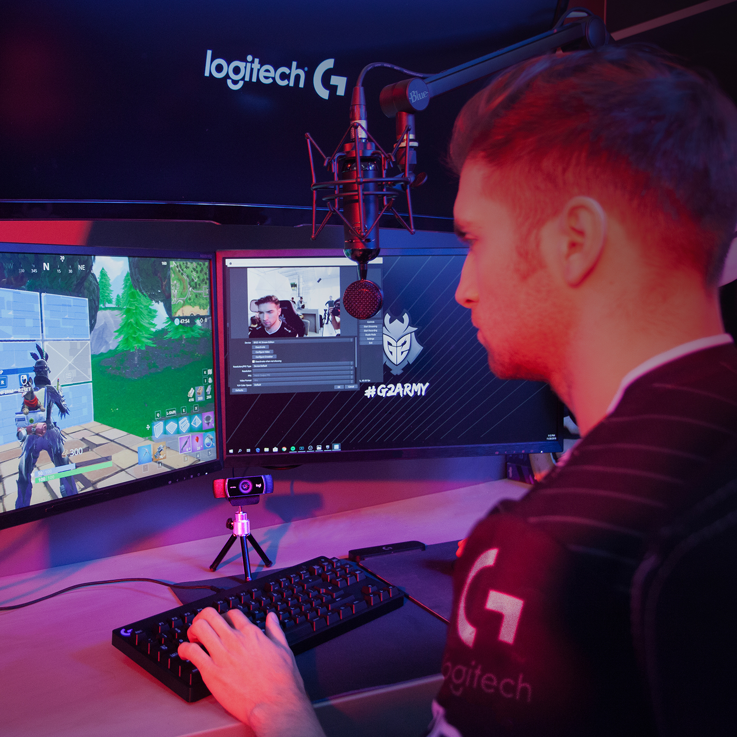 Un homme joue à des jeux vidéo avec deux moniteurs, un micro et une webcam.