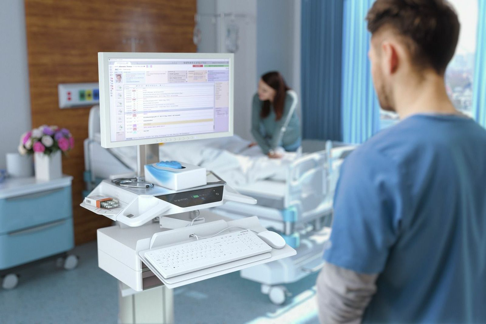 Ein medizinischer Computer auf einem Rollwagen in einem Krankenhauszimmer mit einem Patienten und Arzt.