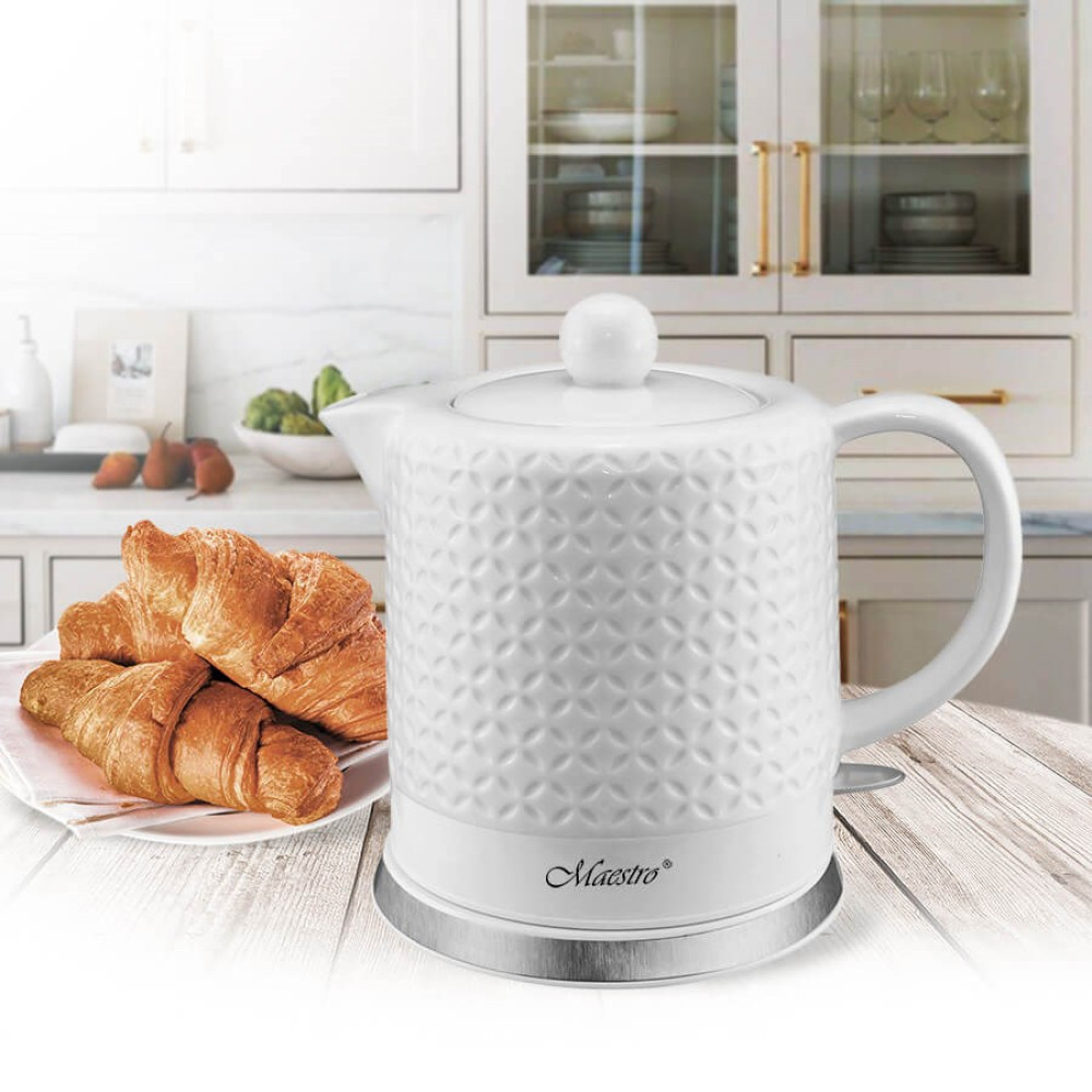 Biały czajnik z wzorem obok rogalików na drewnianym stole.