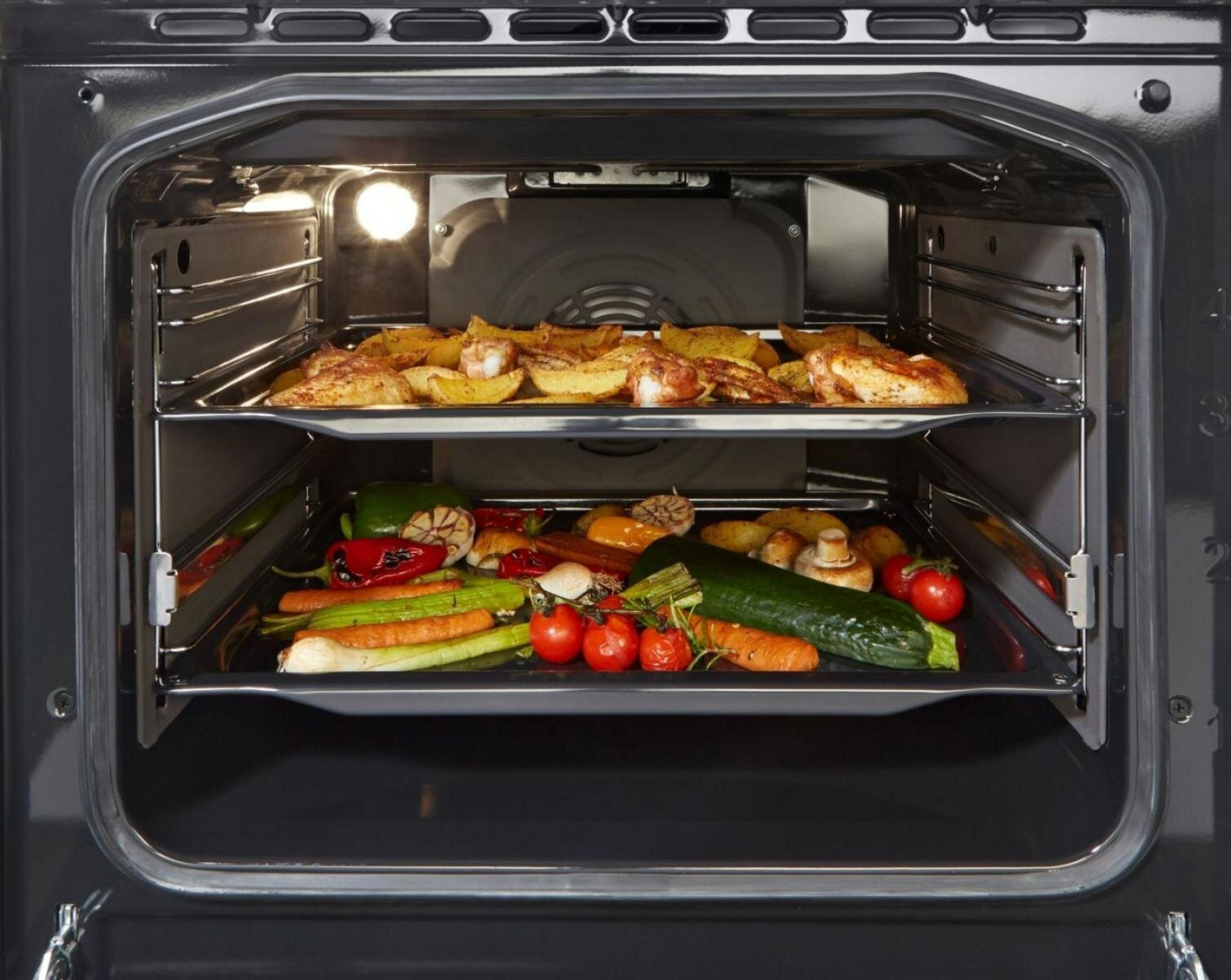 Pollo arrosto e patate sopra verdure in un forno.