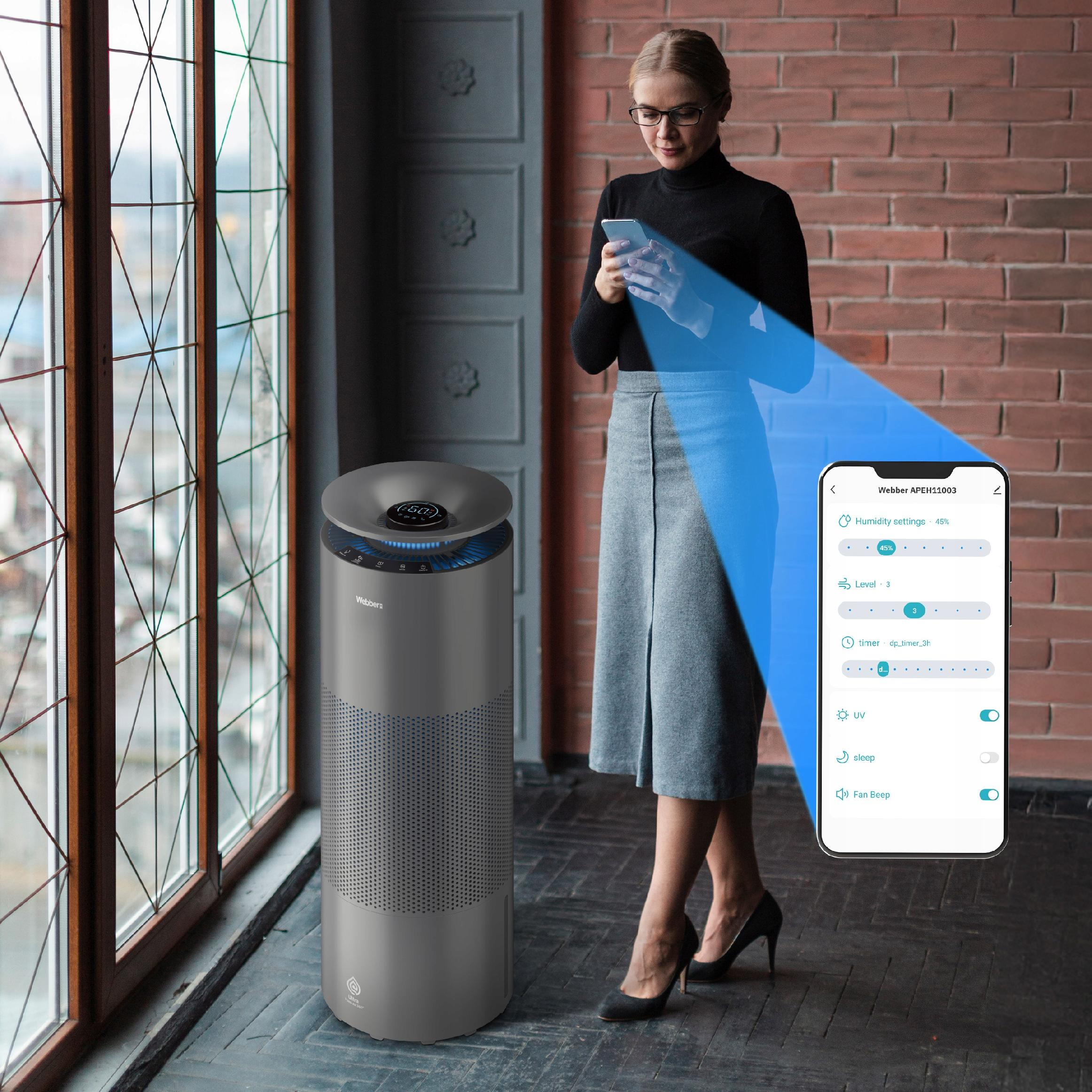 Kobieta obsługuje oczyszczacz powietrza smartfonem w pokoju z ceglanymi ścianami.