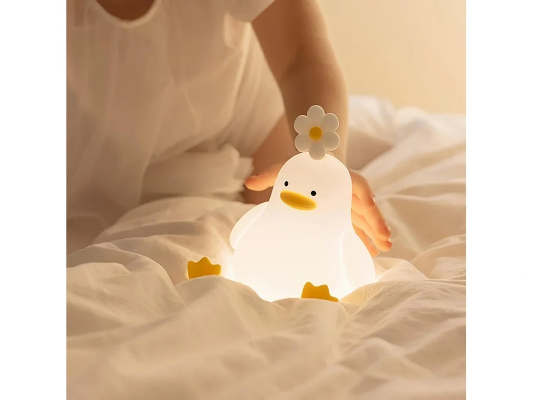 Eine leuchtende weiße Entenlampe mit Blumenaufsatz sitzt auf weißer Bettwäsche.