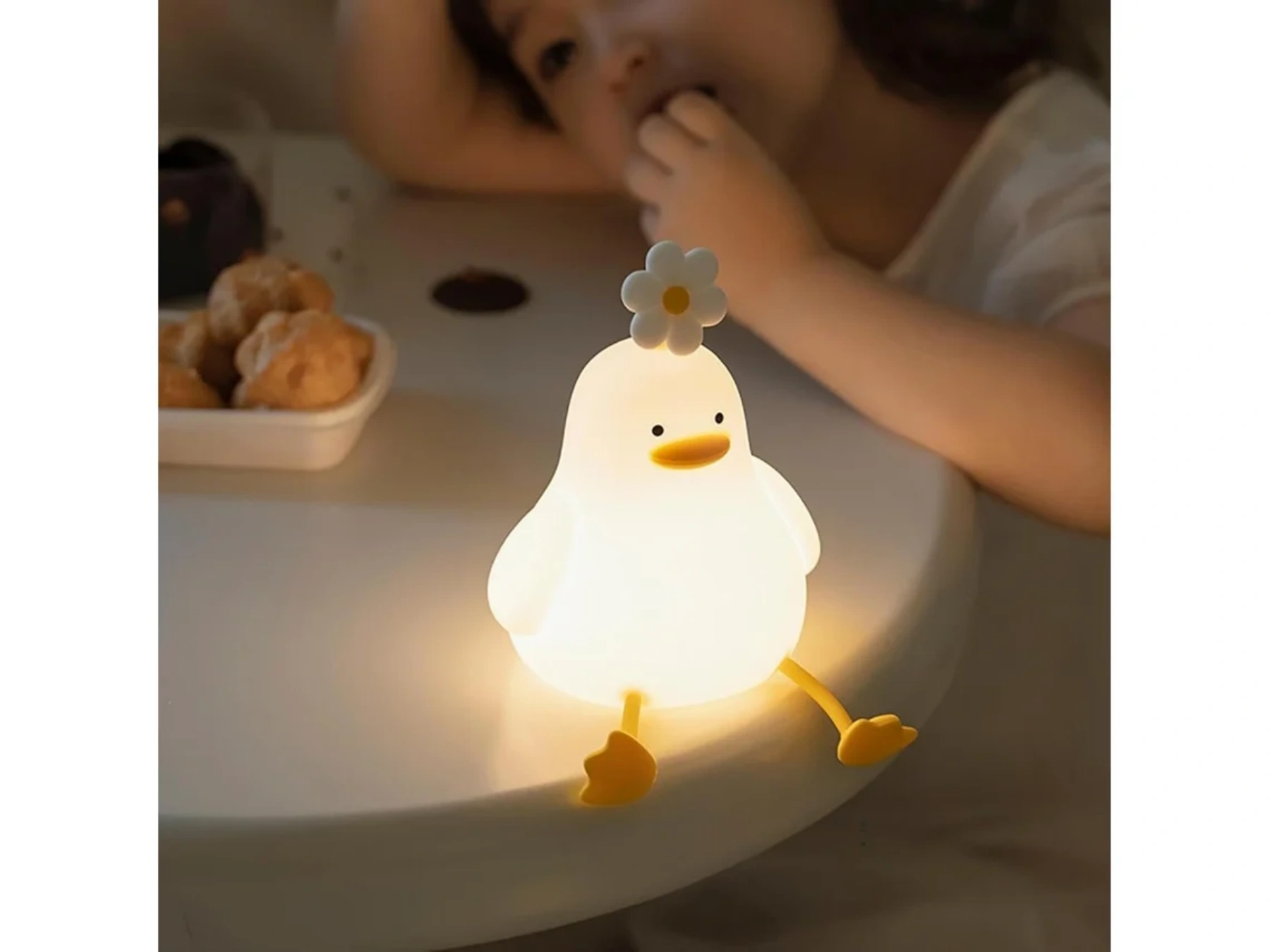 Eine leuchtende Entenlampe mit Blume sitzt auf einem Tisch, neben Schüssel mit Essen.