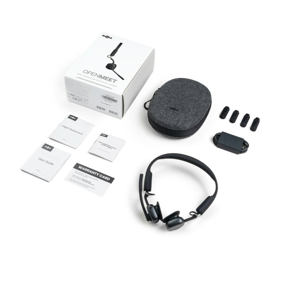 Zestaw słuchawkowy Shokz OpenMeet z akcesoriami do ładowania i instrukcjami na białym tle.