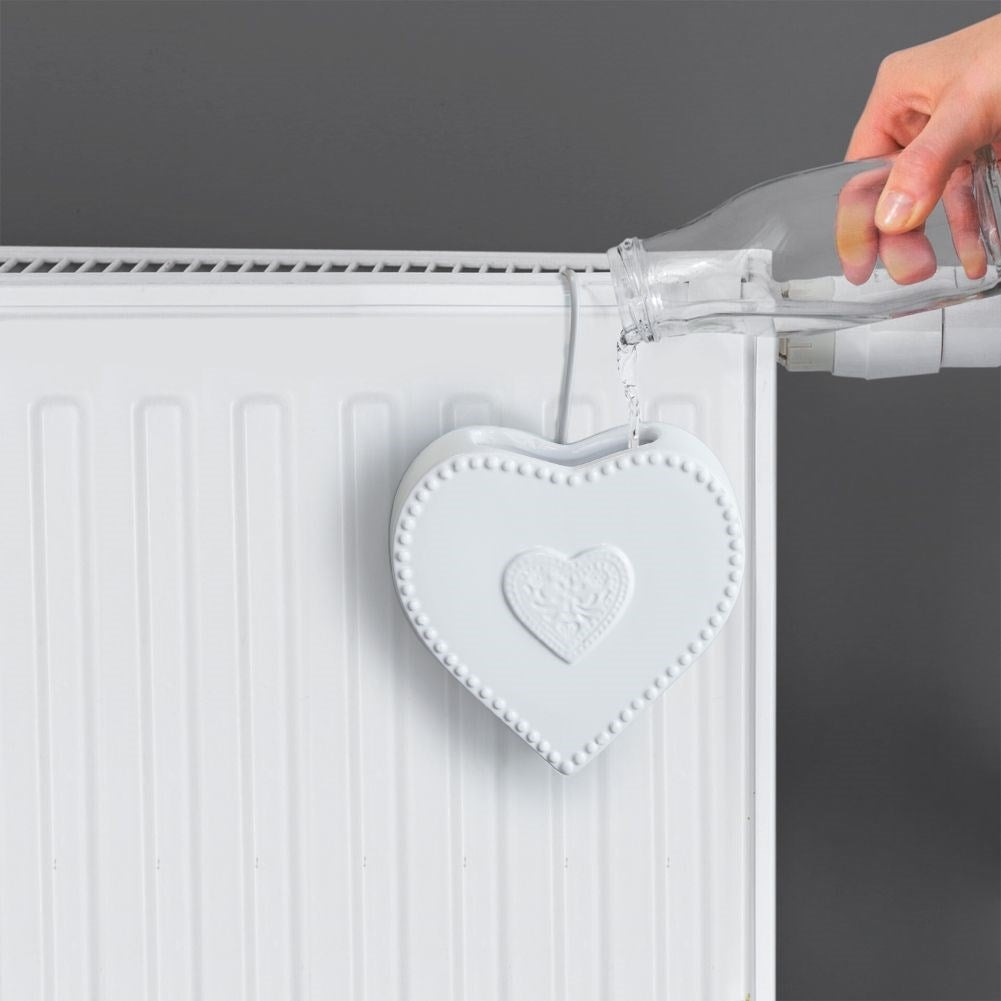 Un humidificador de cerámica blanco en forma de corazón se sujeta a un radiador, vertiendo agua.