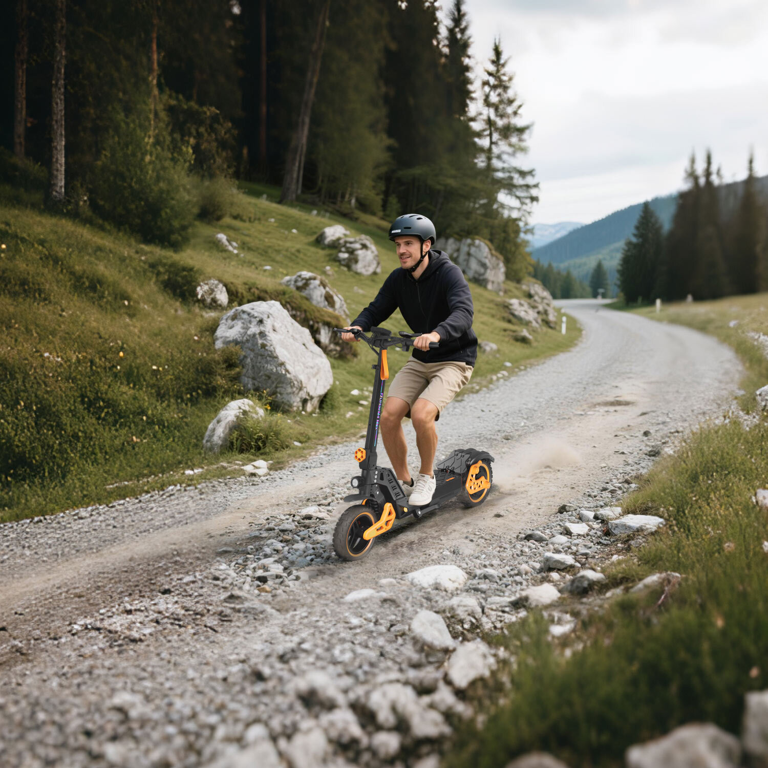 Mężczyzna jedzie na hulajnodze elektrycznej po żwirowej drodze w górach, wzbijając kurz.