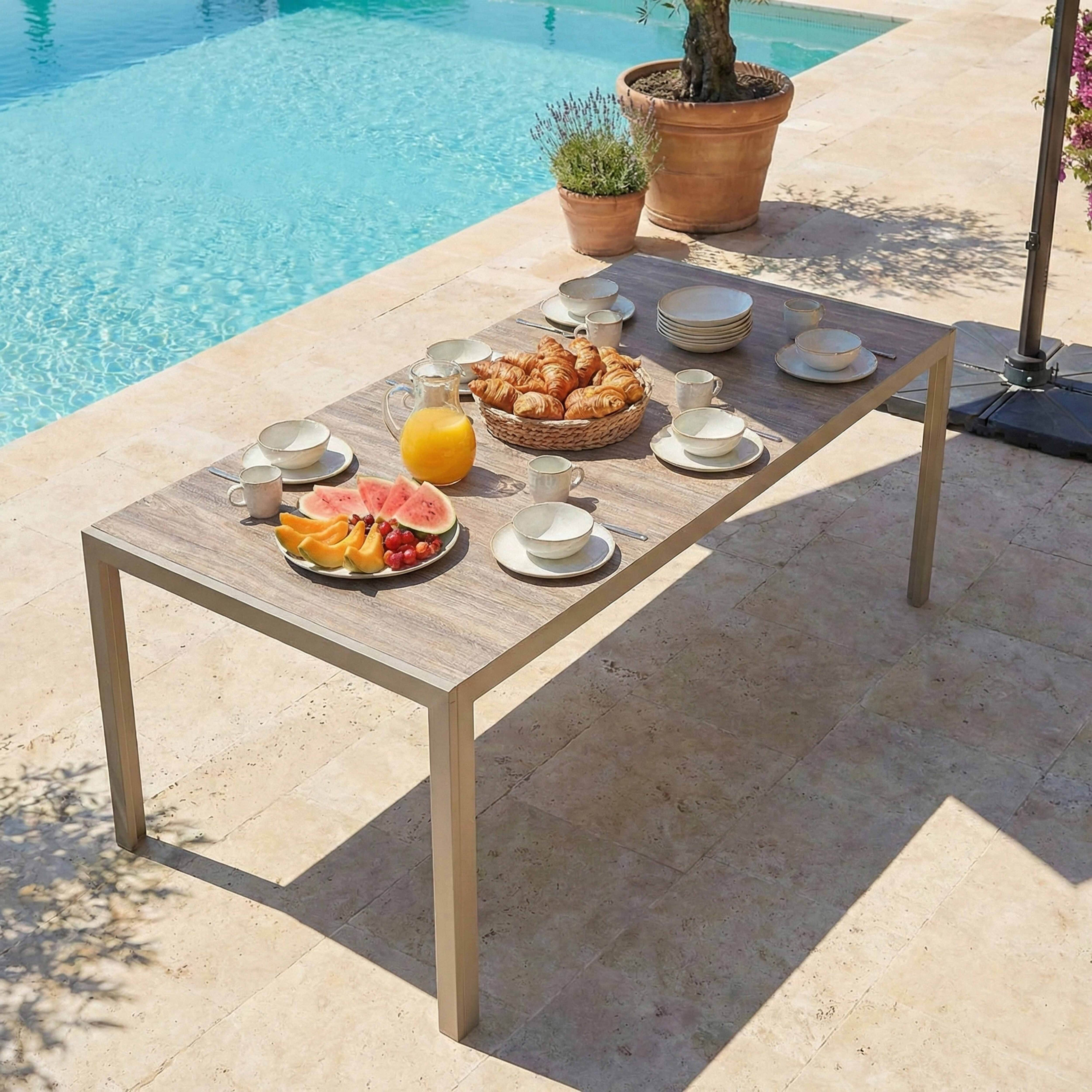 Ein Frühstückstisch mit Croissants, Obst und Orangensaft neben einem Pool.