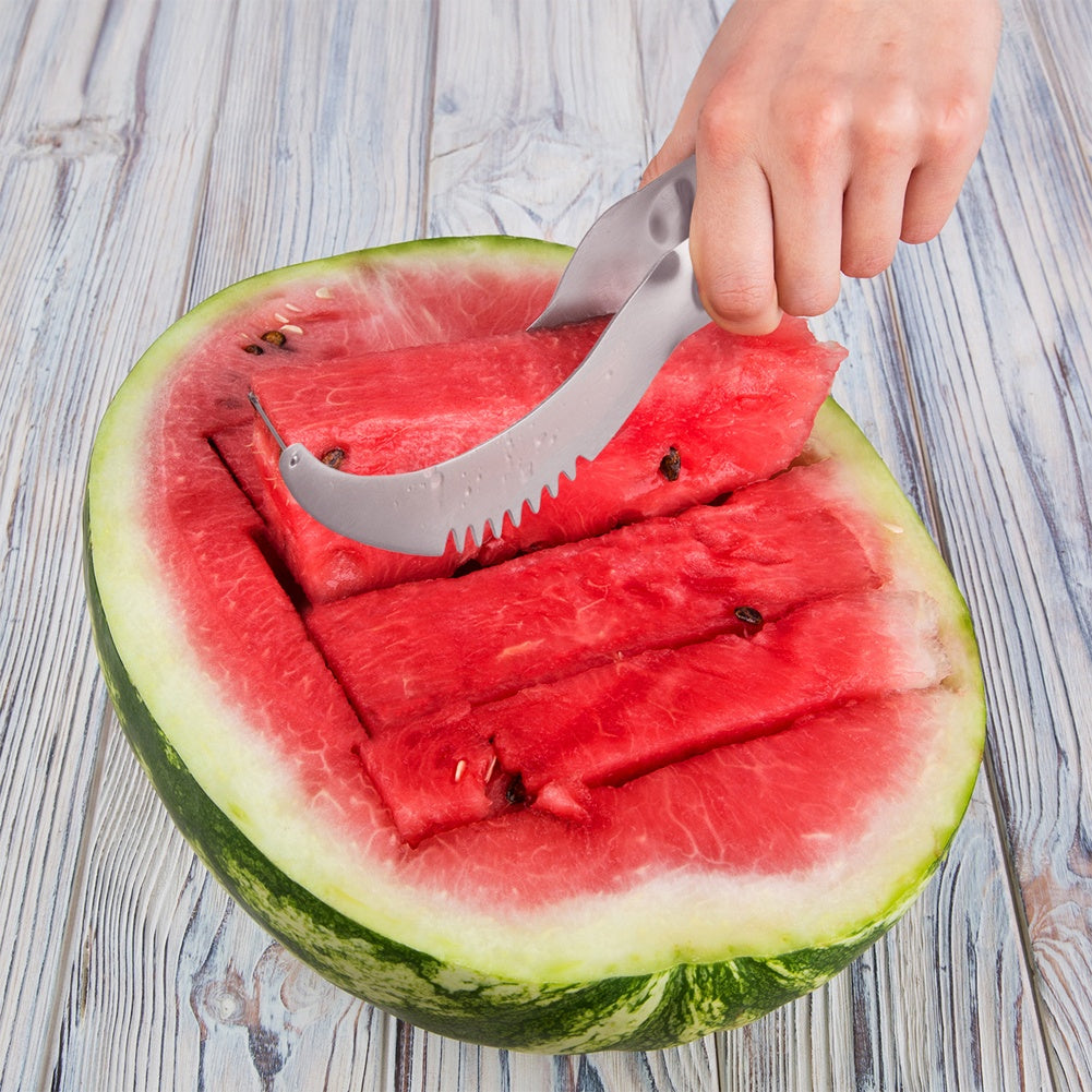 Una mano usa un cuchillo curvo para cortar una sandía madura sobre una mesa de madera.