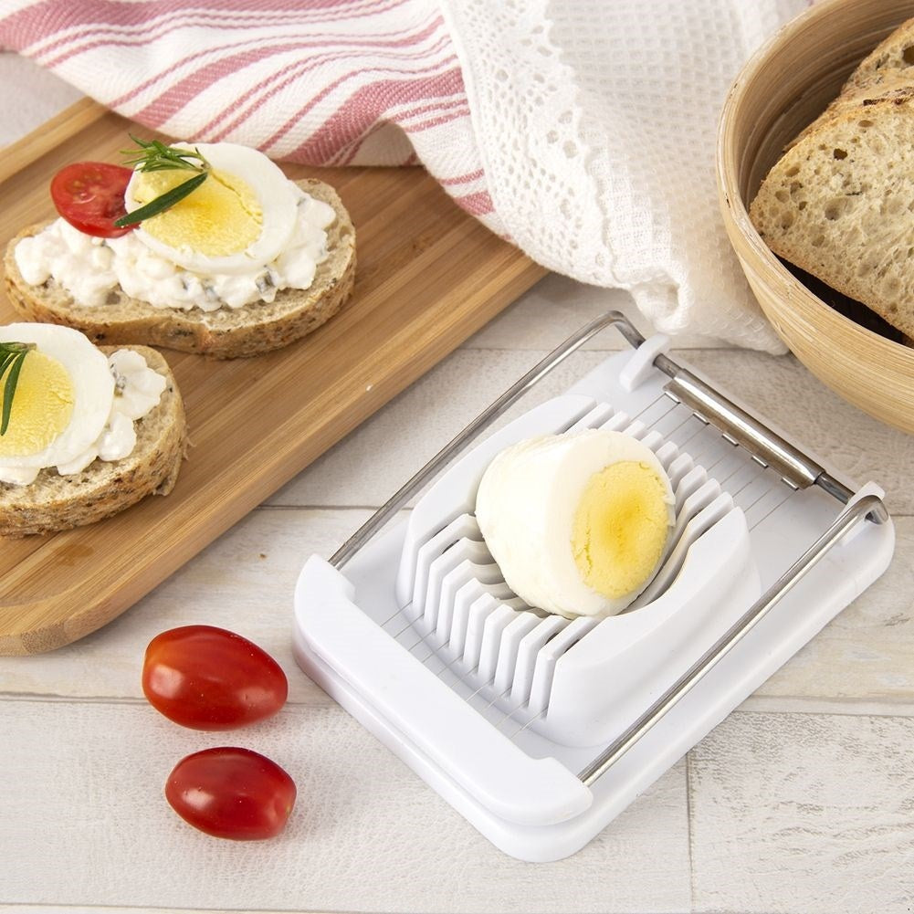 Un huevo duro se corta en un cortador de huevos. Hay tomates y rebanadas de pan cerca.
