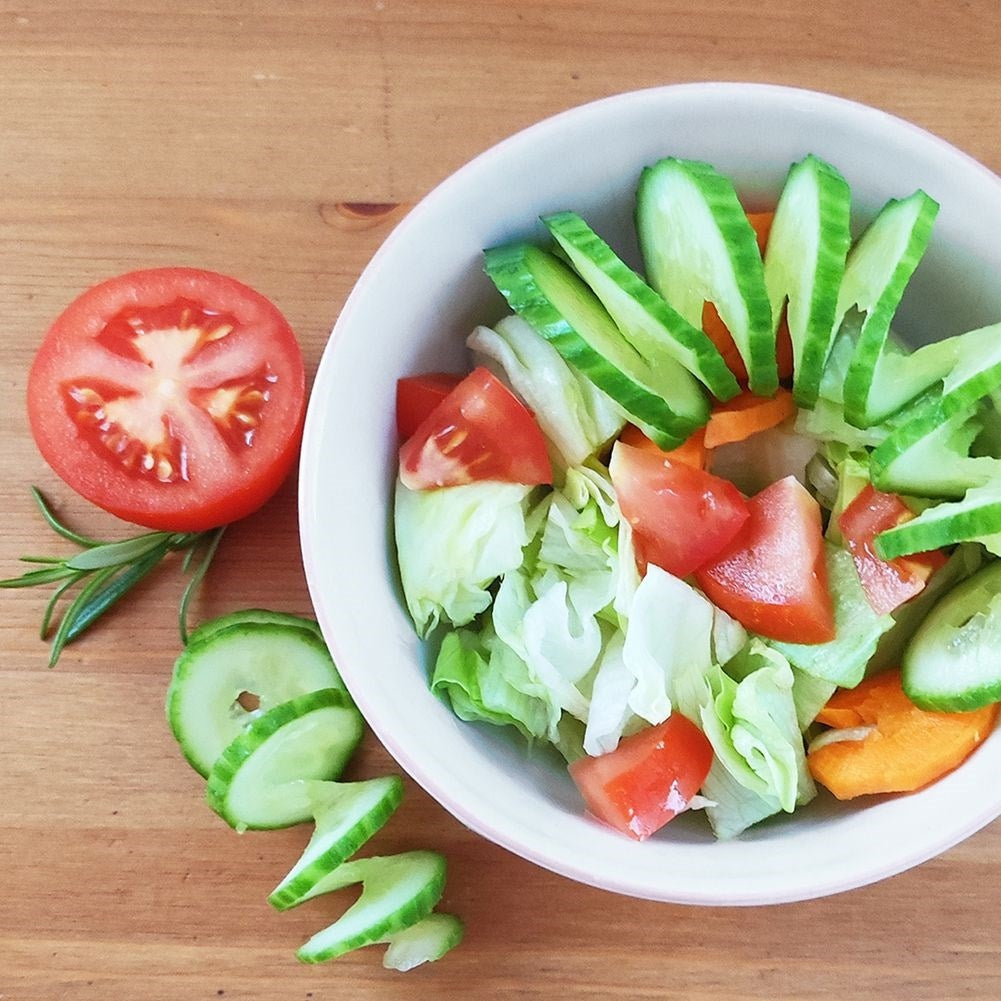 Ensalada fresca con tomates, pepinos y lechuga en mesa de madera.