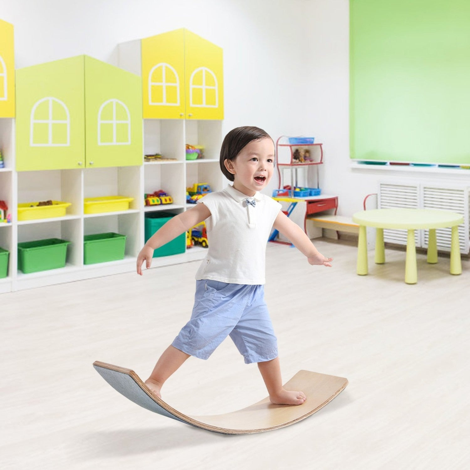 Un niño pequeño se balancea en una tabla de madera en una sala de juegos con estantes de juguetes.