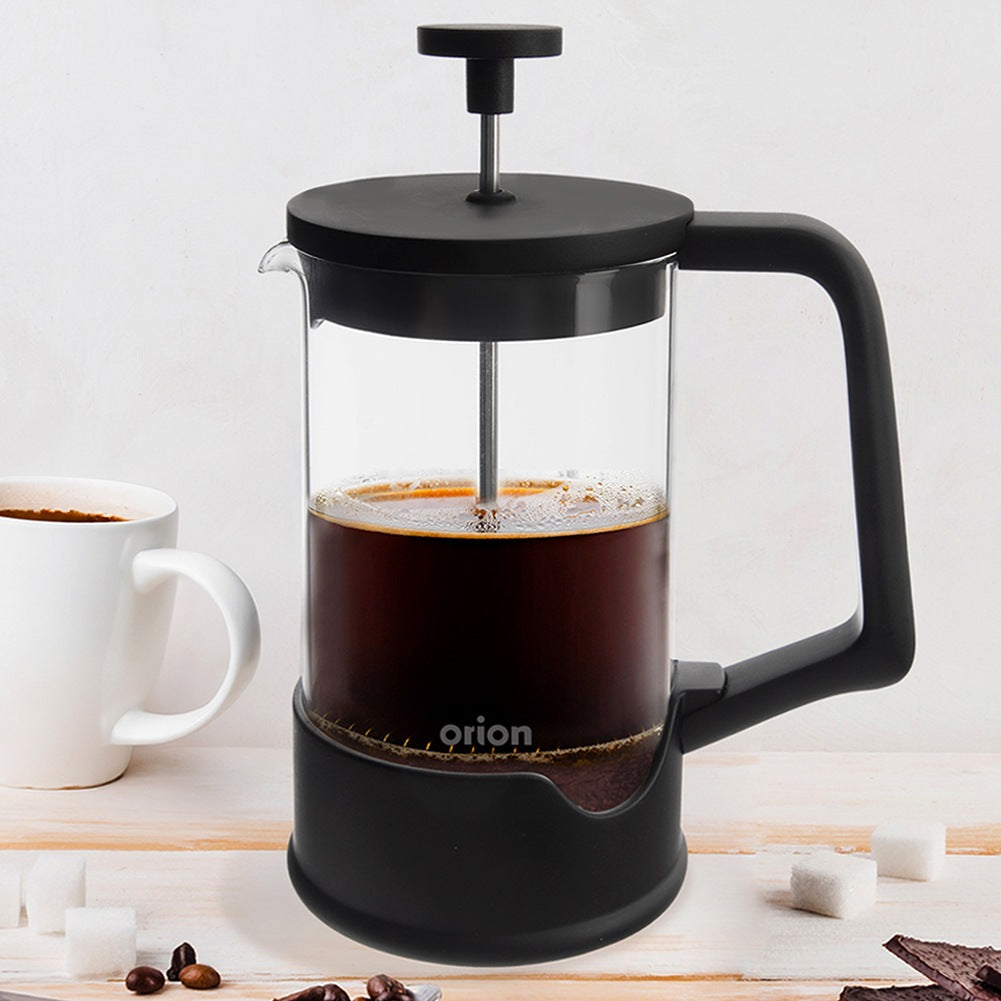 Prensa francesa negra con café junto a una taza blanca.