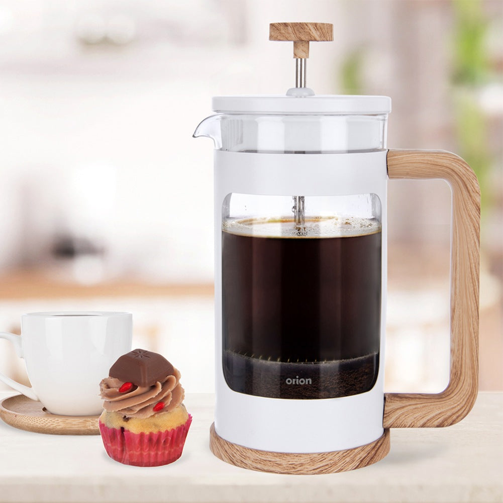 Prensa francesa con café, taza y cupcake sobre una mesa.