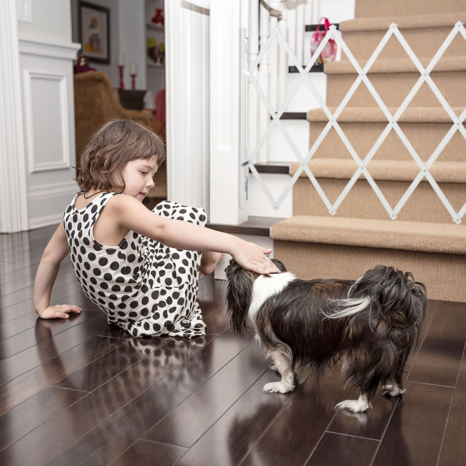 Una niña con vestido de lunares acaricia un perro en el suelo.