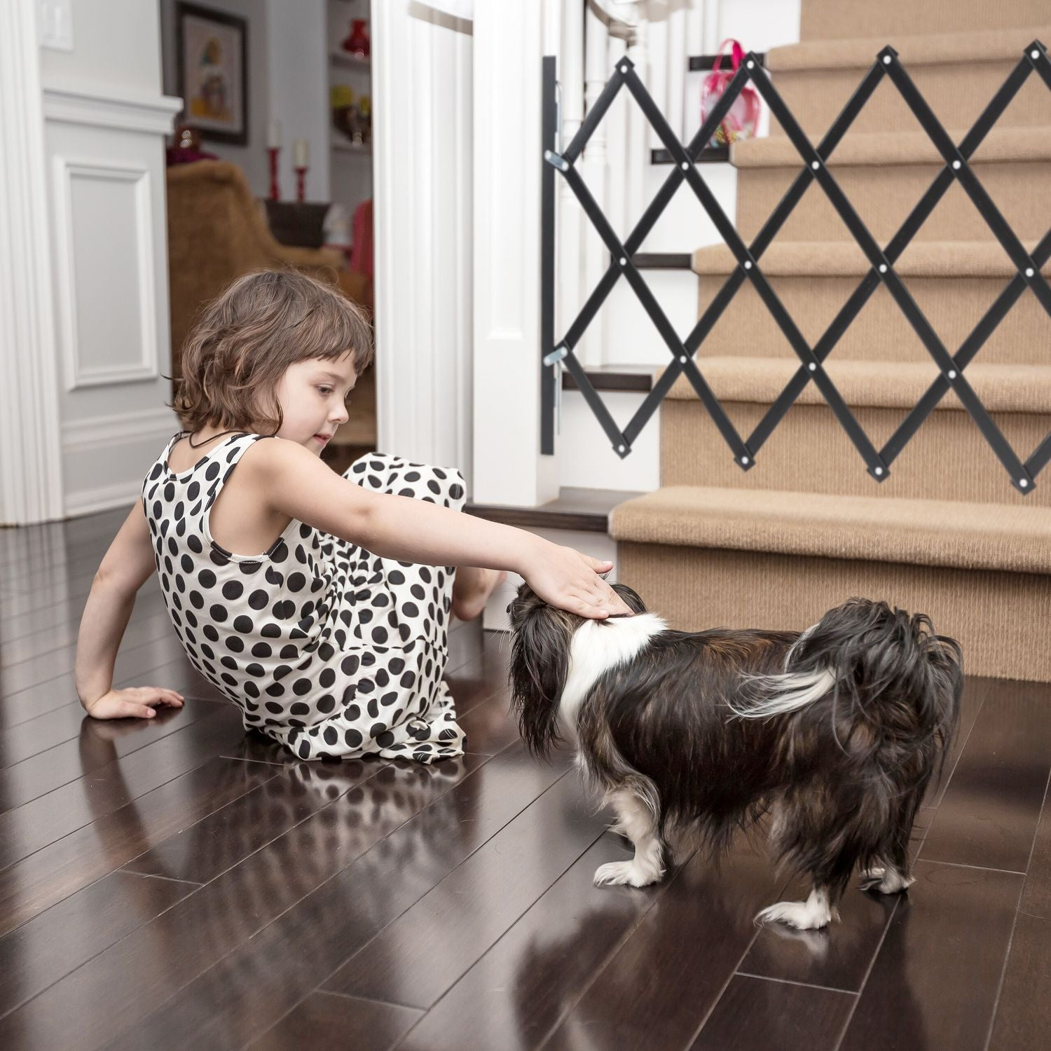 Una niña con vestido de lunares acaricia a un perro peludo en suelo de madera.
