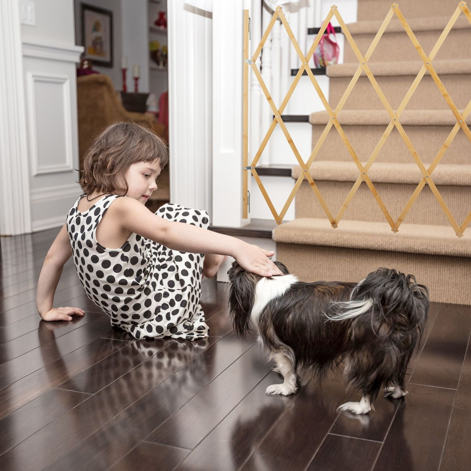 Una niña con vestido de lunares acaricia a un perro junto a una escalera con puerta de madera.