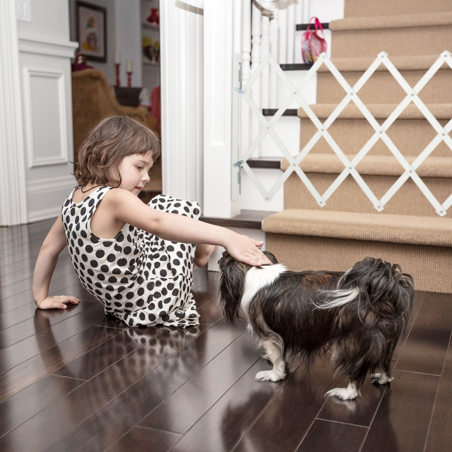Una niña con vestido de lunares acaricia a un perro en suelo de madera oscura.