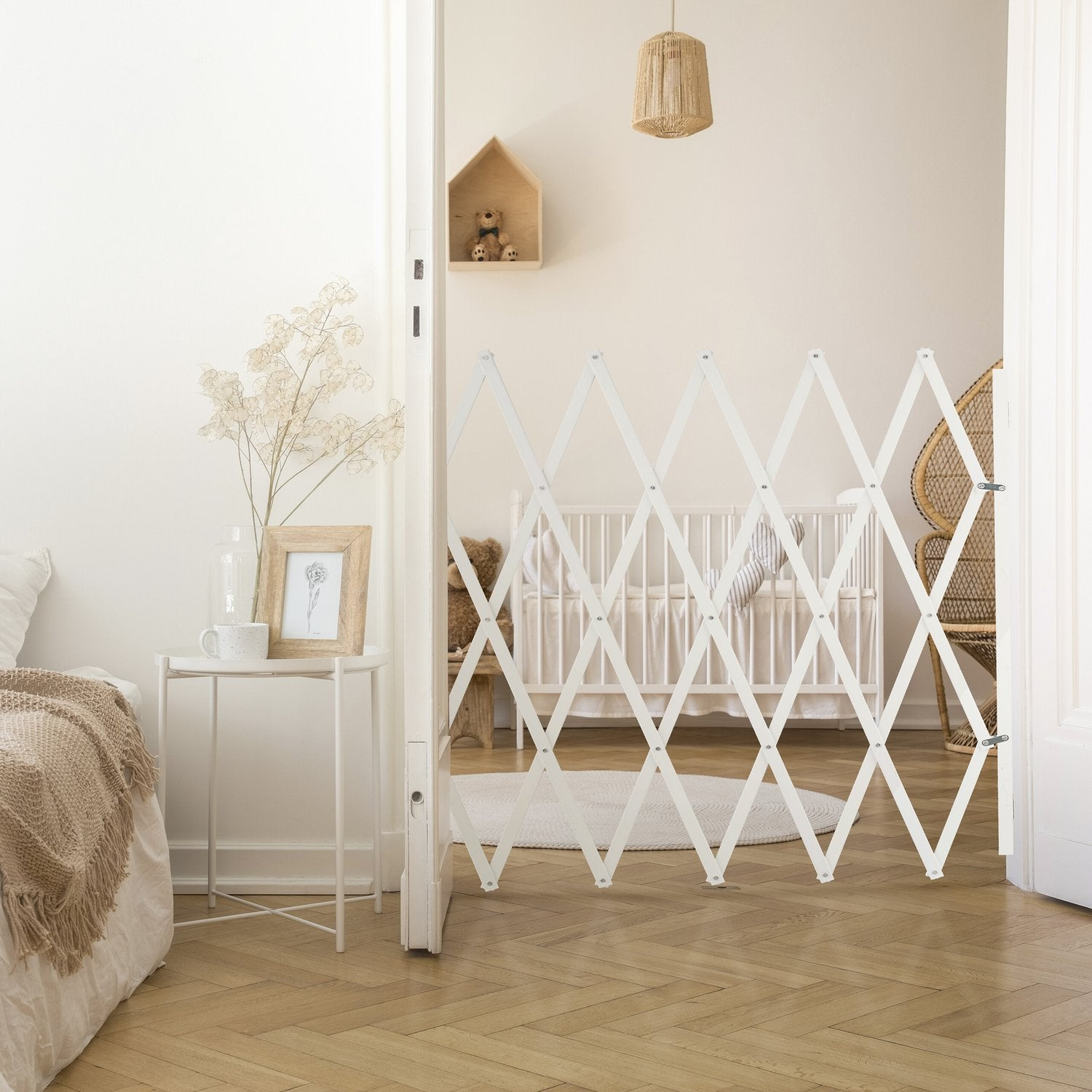 Una barrera blanca de acordeón divide un dormitorio con cuna, mesa auxiliar y sillón. Suelo de madera.