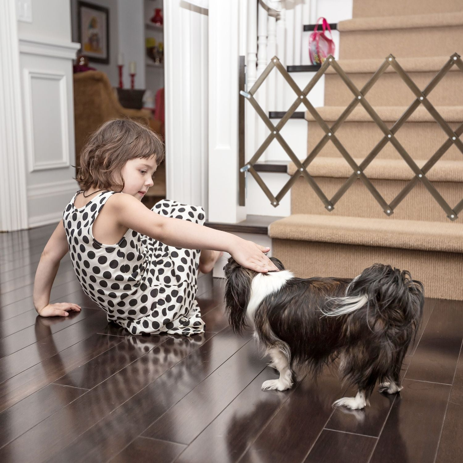 Una niña con vestido de lunares acaricia a un perro en suelo de madera oscura.