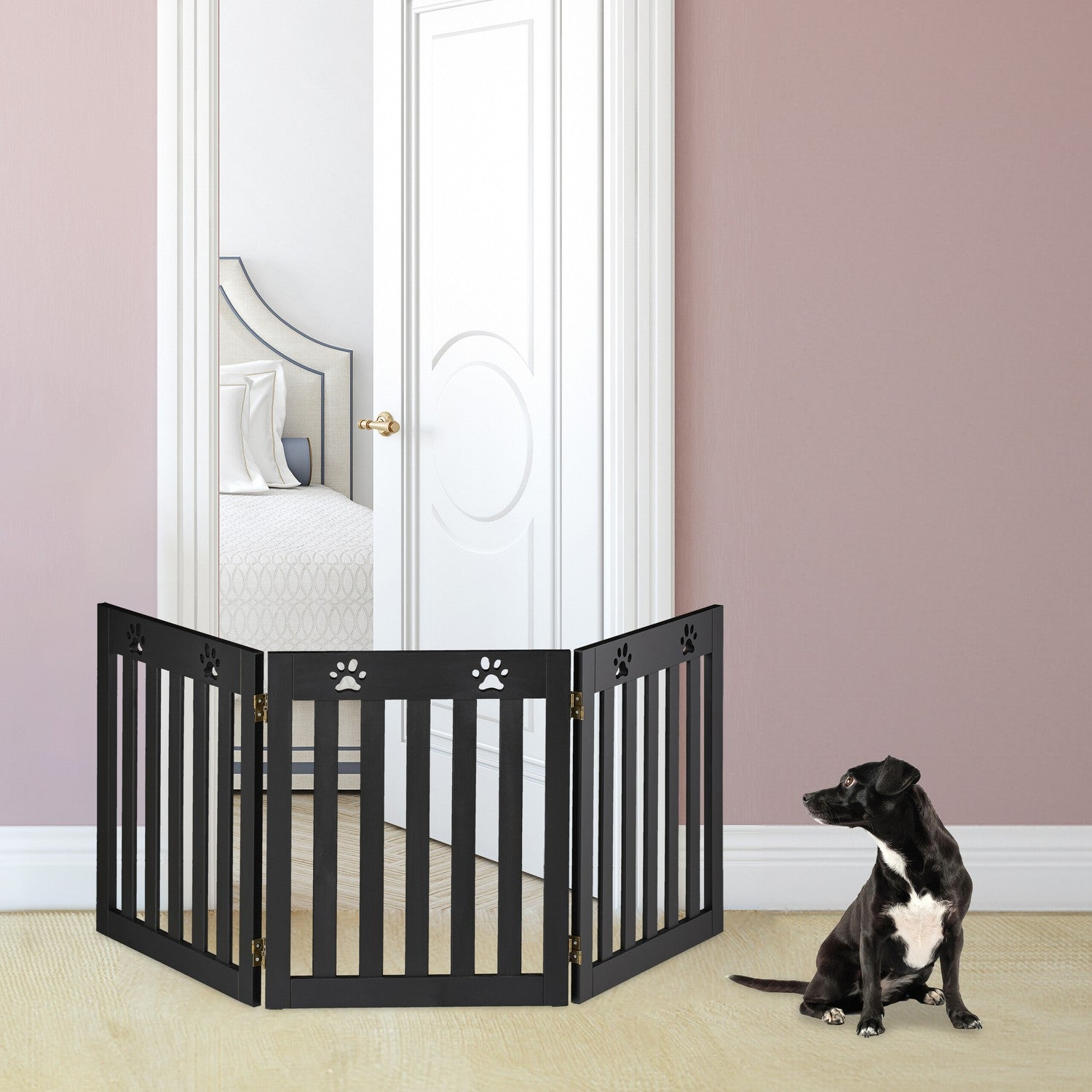 Un perro negro se sienta ante una barrera de madera negra en una puerta abierta.