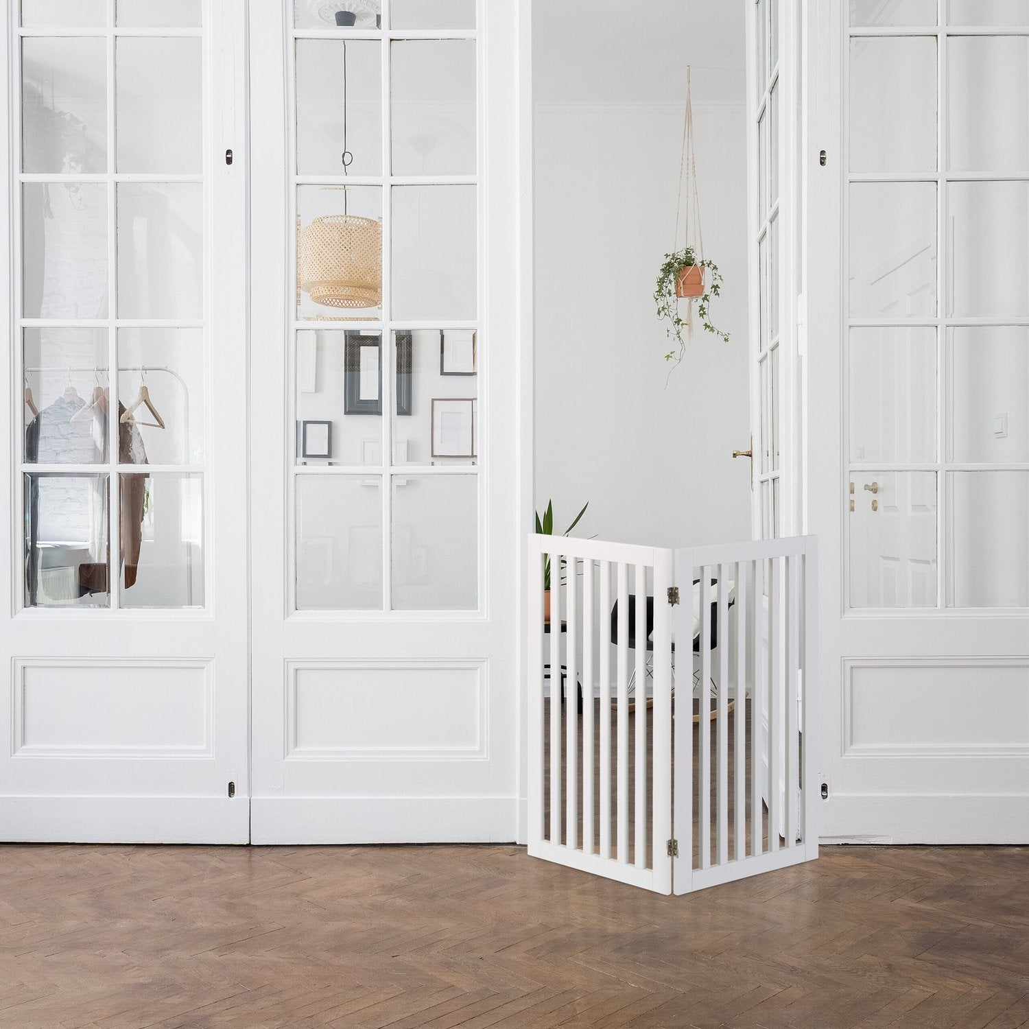Una barrera blanca para bebés se alza sobre suelo de madera ante puertas de cristal blancas.