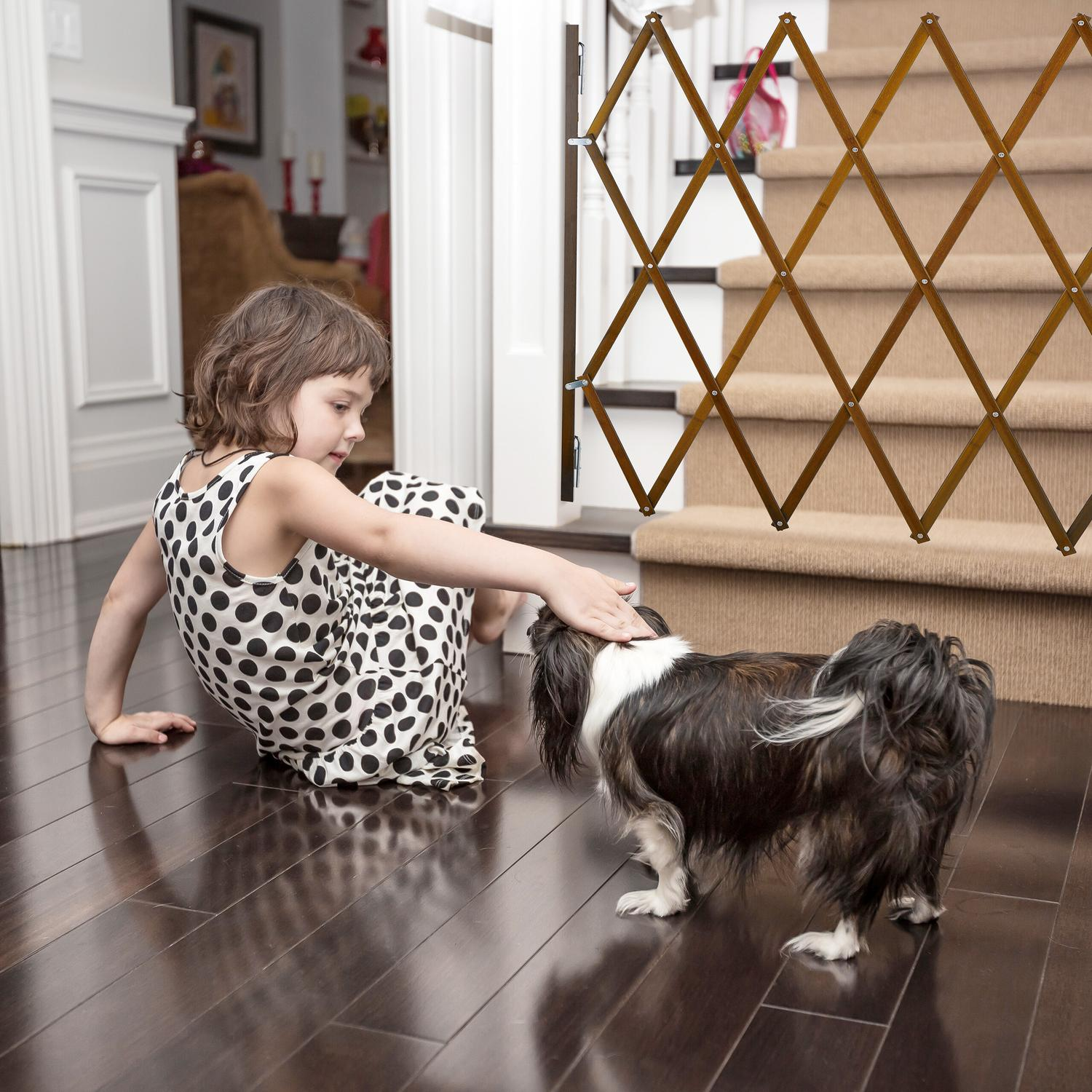 Una niña con vestido de lunares acaricia a un perro cerca de una escalera con puerta de madera.