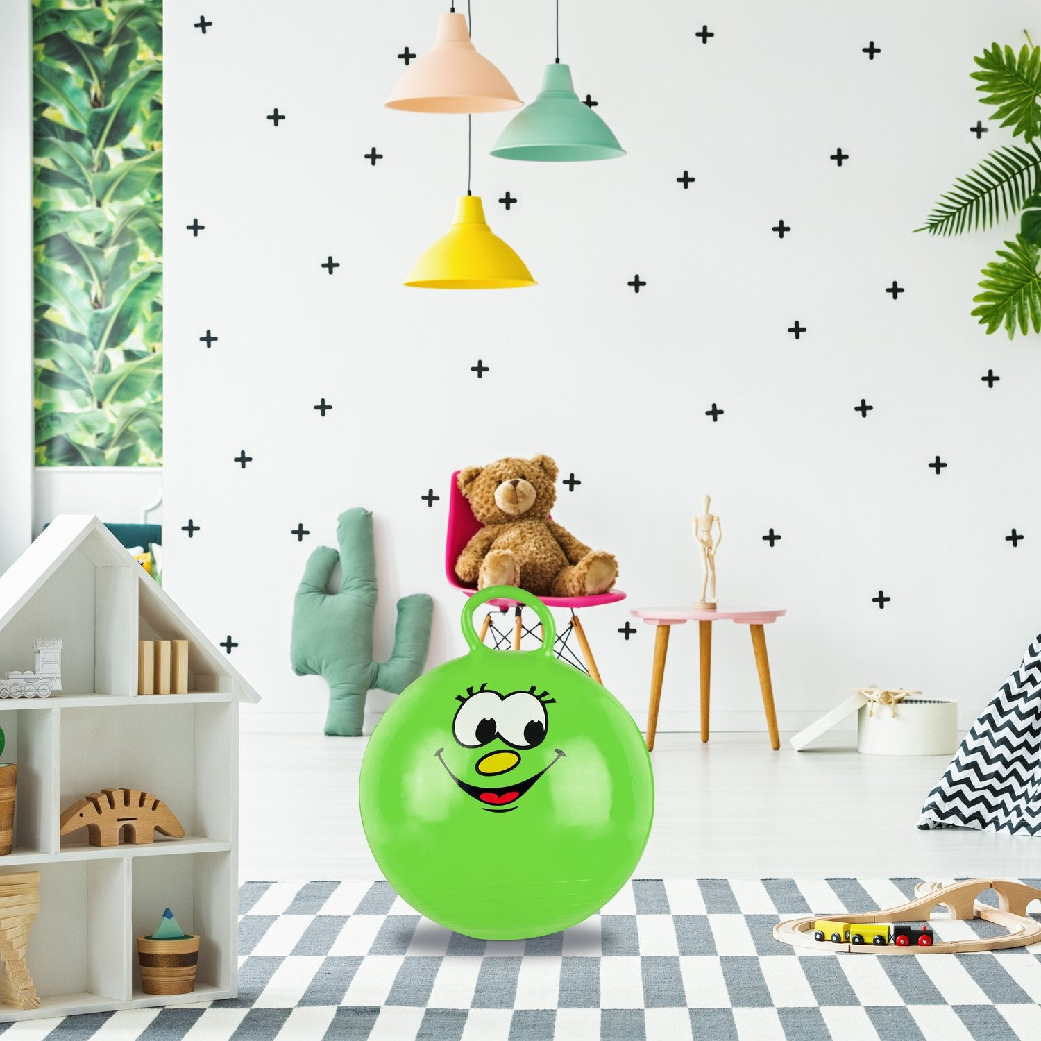 Una pelota saltarina verde con cara está sobre una alfombra. Un oso de peluche está sentado.