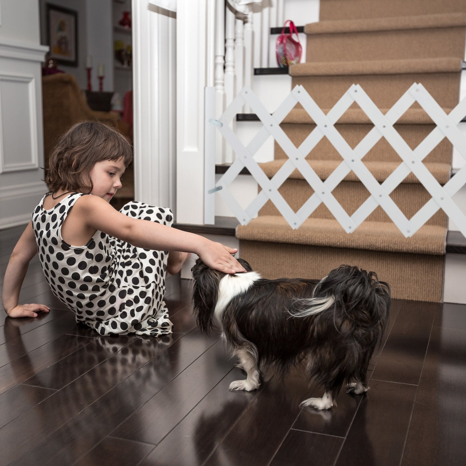 Una niña con vestido de lunares acaricia un perro frente a una escalera con valla.