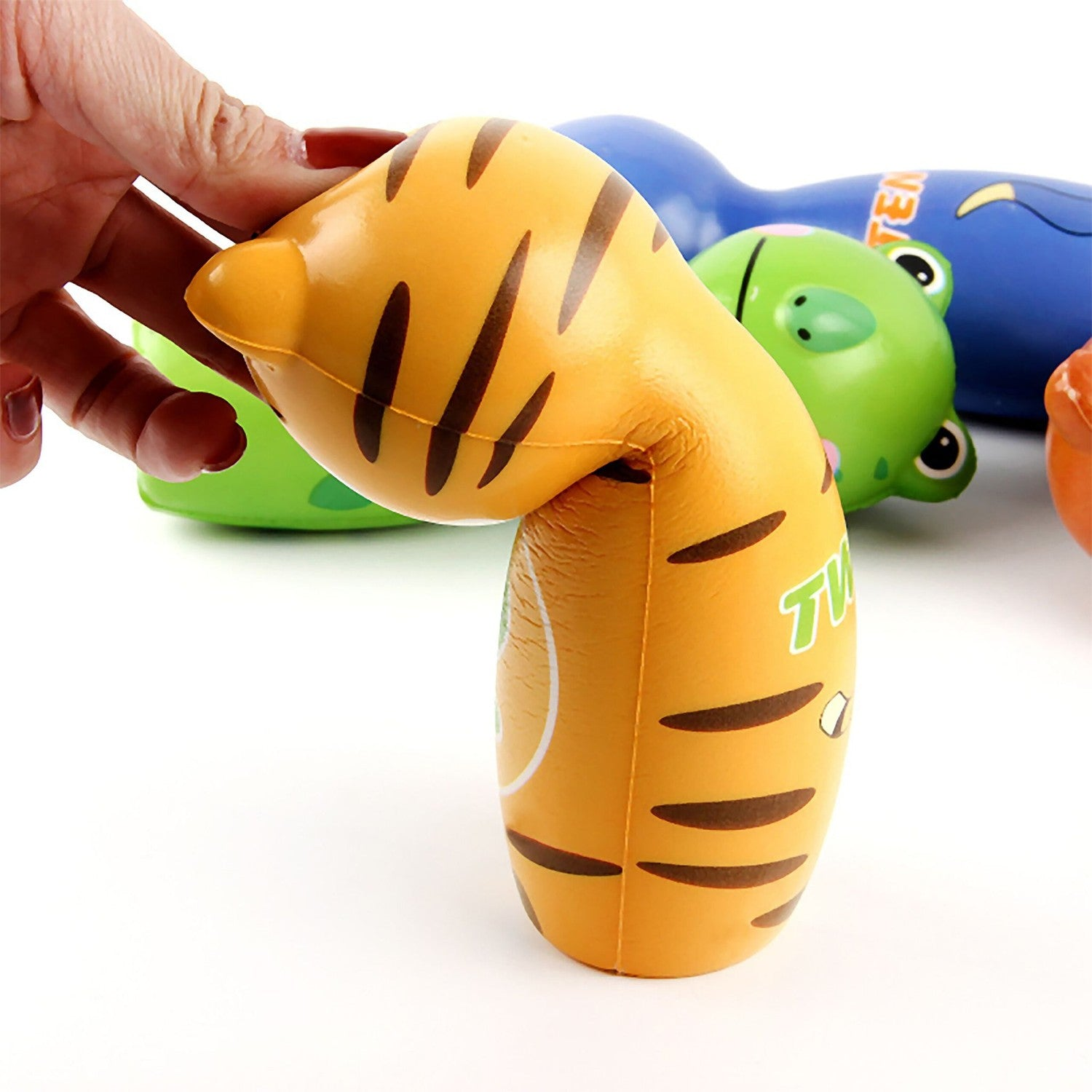 Una mano aprieta una pelota naranja con rayas de tigre. Pelotas verdes y azules al fondo.
