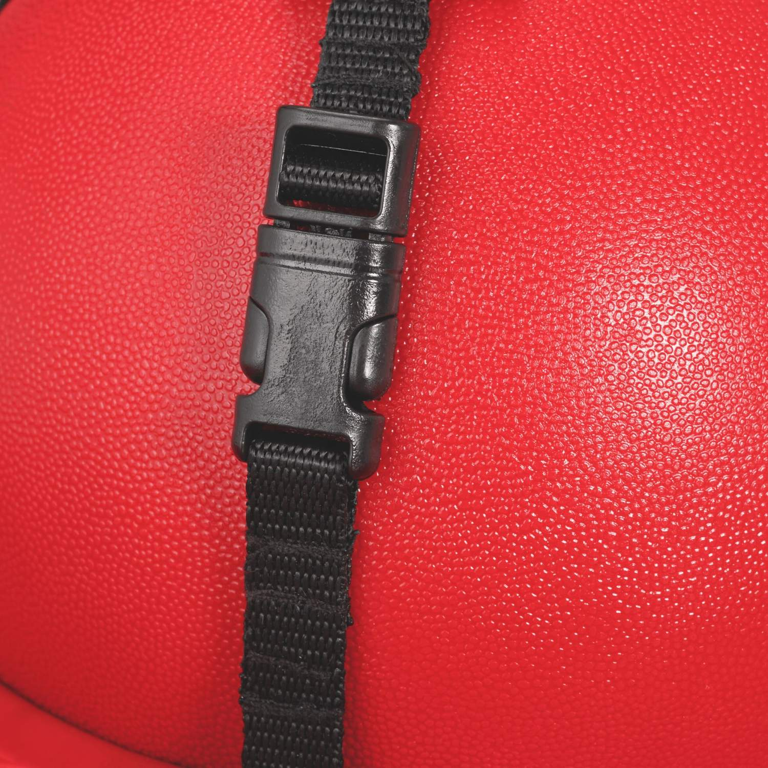 Primer plano de una hebilla y correa negras sobre una superficie roja texturizada.