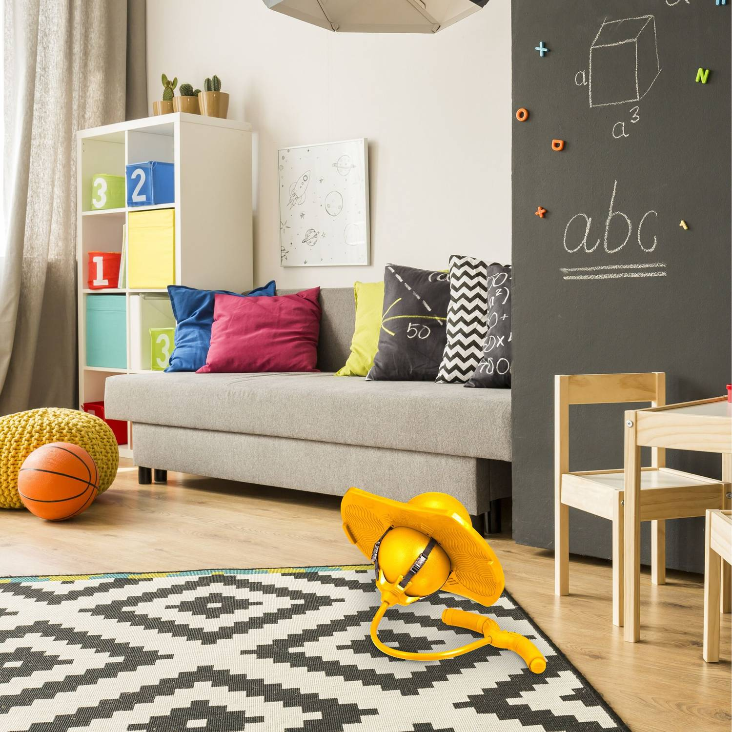 Habitación infantil con sofá, juguetes y pizarra. Sombrero amarillo en la alfombra.