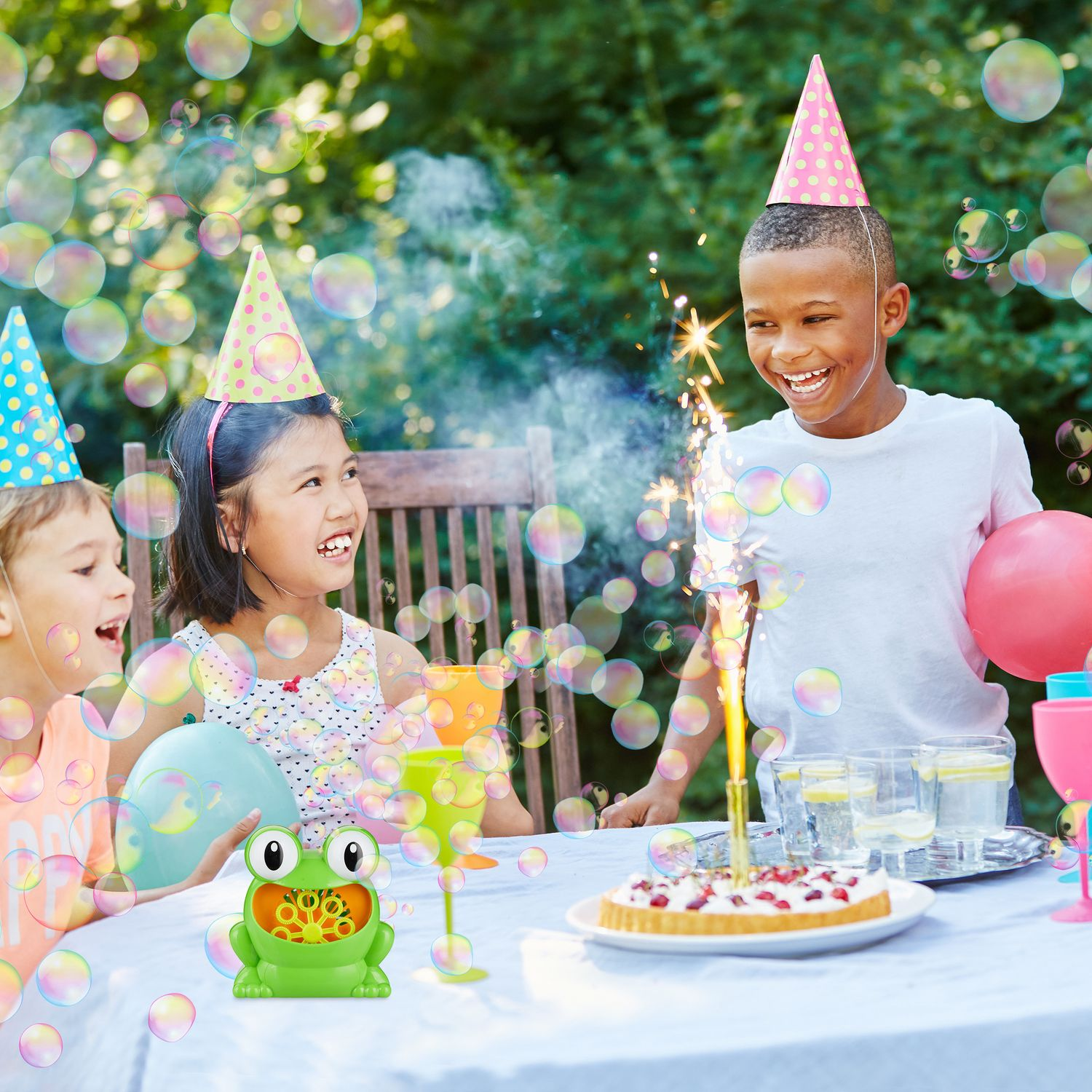 Niños con sombreros de fiesta celebran al aire libre con pastel, burbujas y chisperos.
