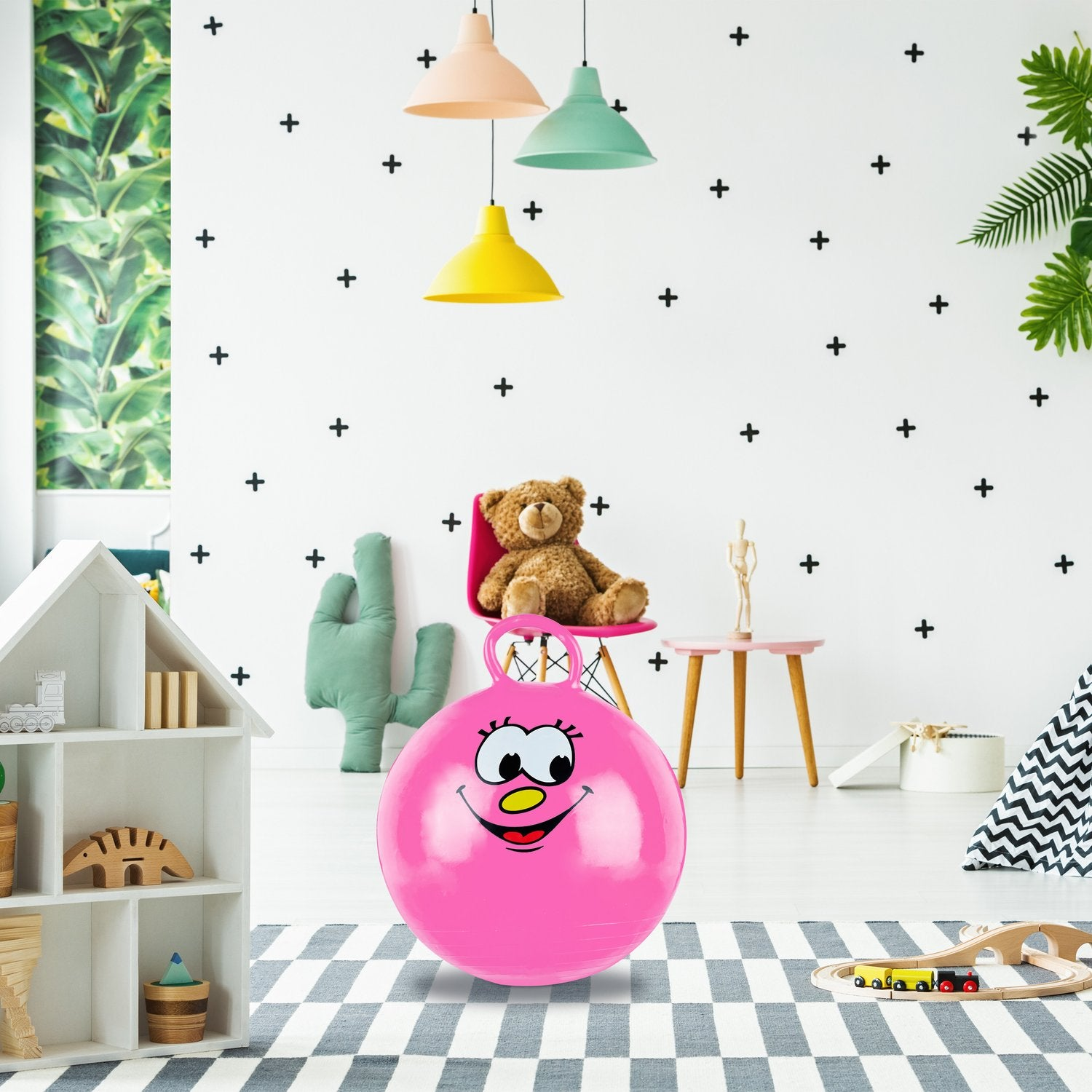 Una pelota saltarina rosa con cara se sienta sobre una alfombra en una habitación infantil.