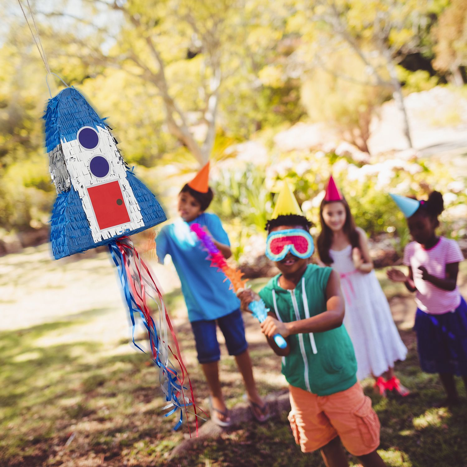 Niños juegan con una piñata de cohete al aire libre, uno tiene los ojos vendados.
