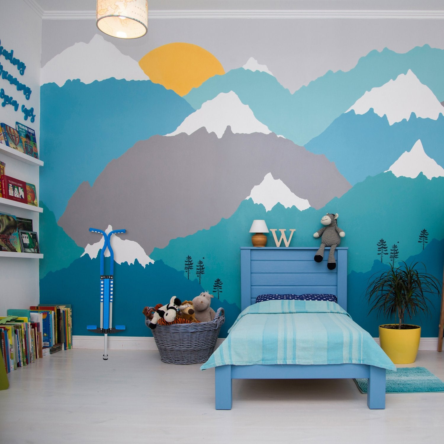 Dormitorio infantil con mural de montaña, cama azul, juguetes y libros.