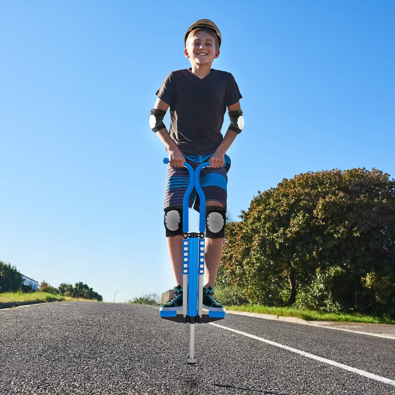 Un niño en un pogo stick azul baja por una calle, vistiendo equipo de protección.