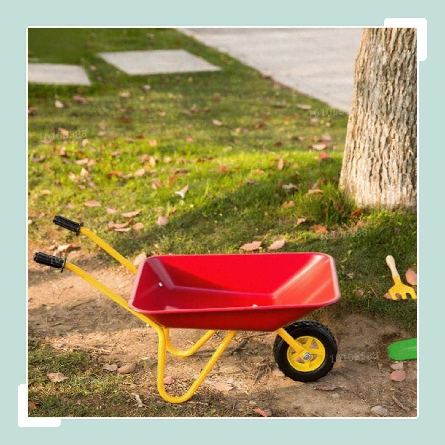 Una carretilla roja con marco amarillo está sobre hierba junto a un árbol.