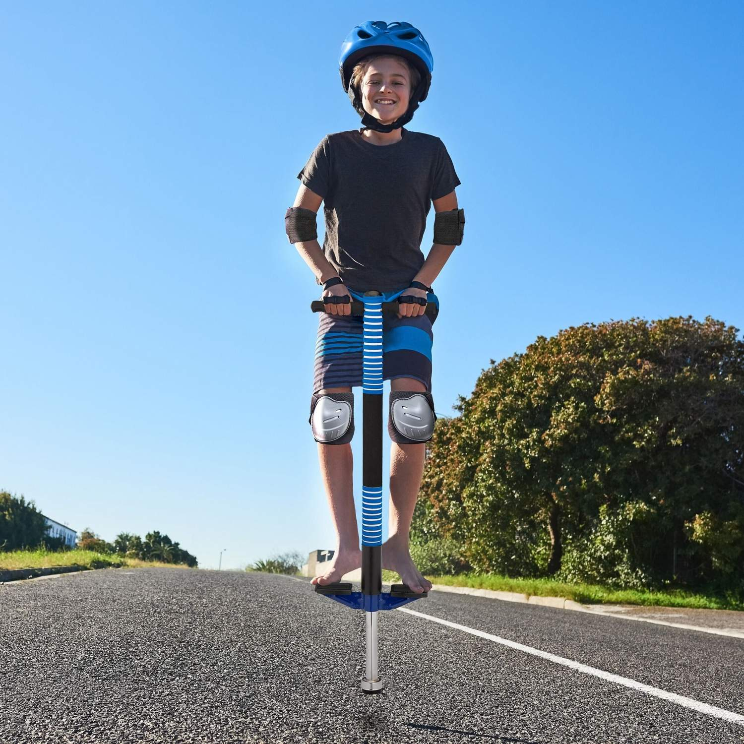 Chico con casco saltando en un palo de pogo azul en una carretera.